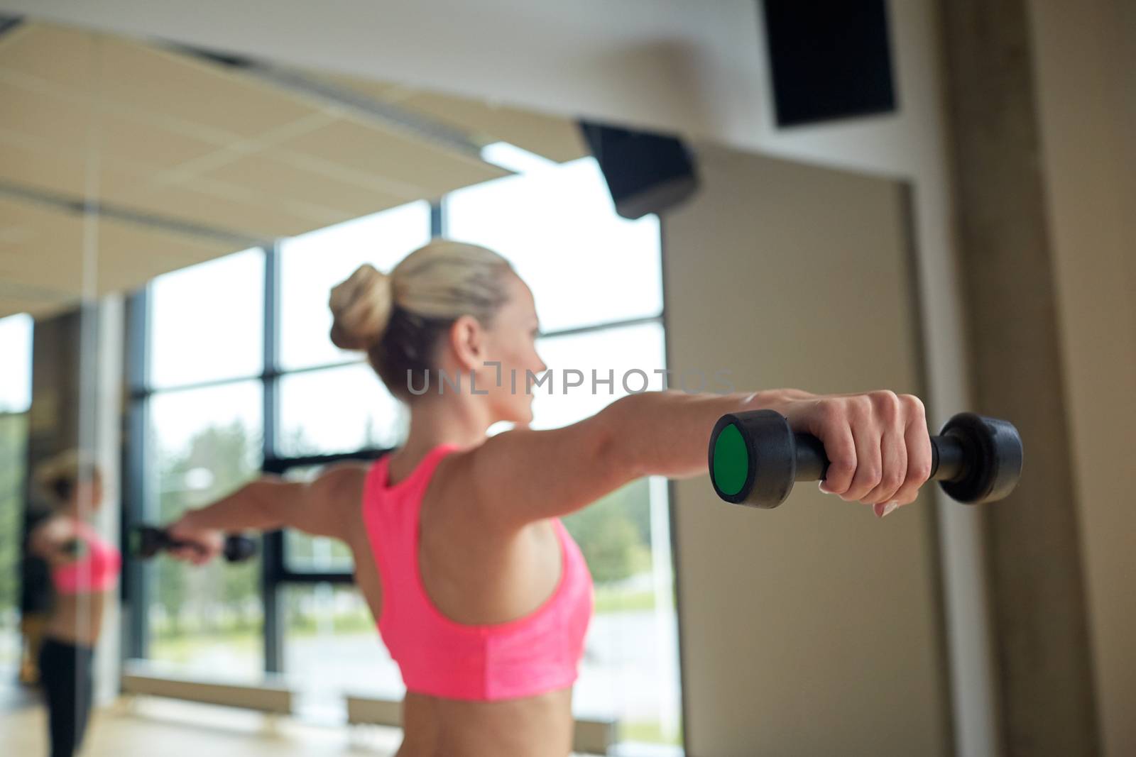 woman with dumbbells flexing muscles in gym by dolgachov