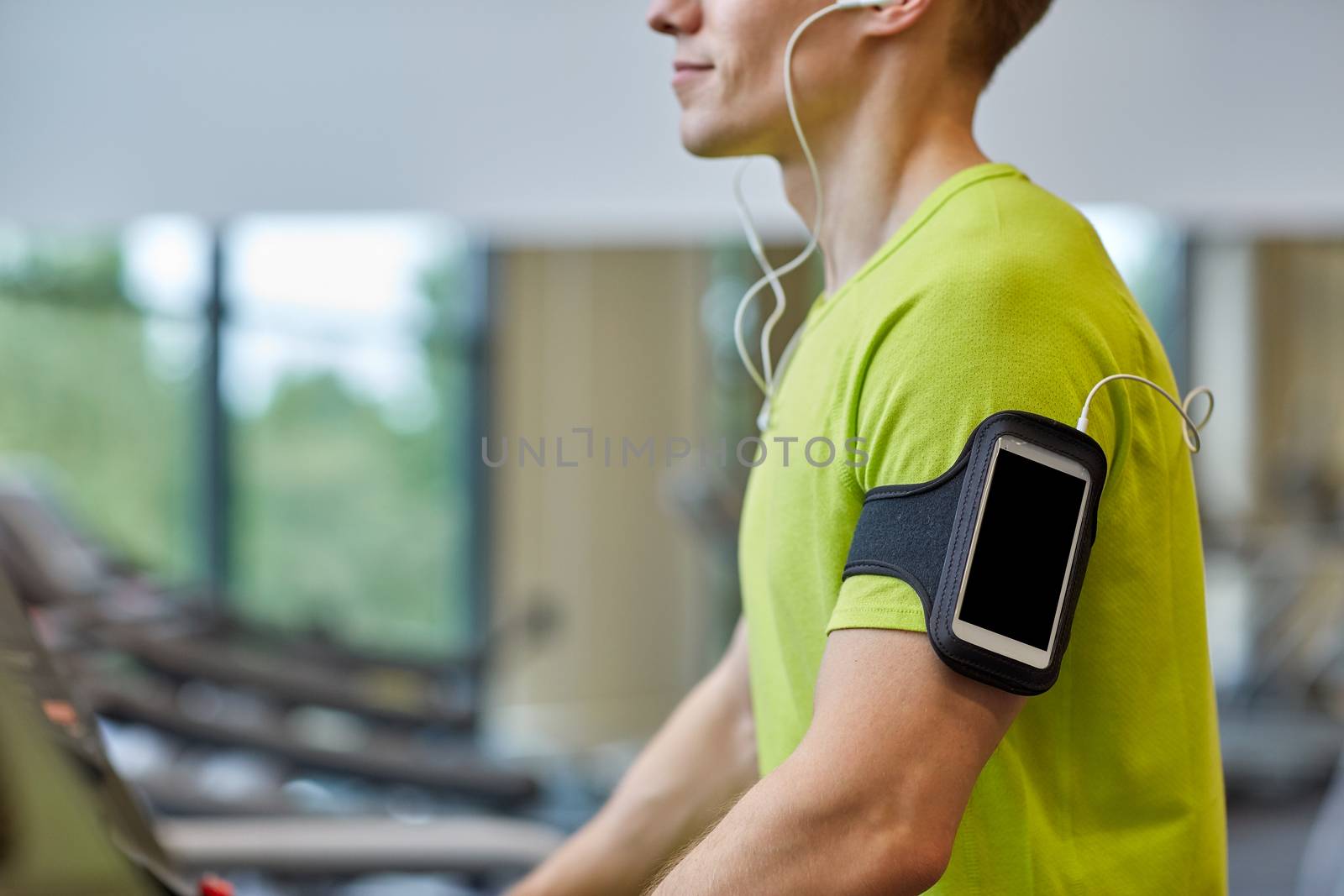 sport, fitness, lifestyle, technology and people concept - close up of man with smartphone and earphones exercising on treadmill in gym
