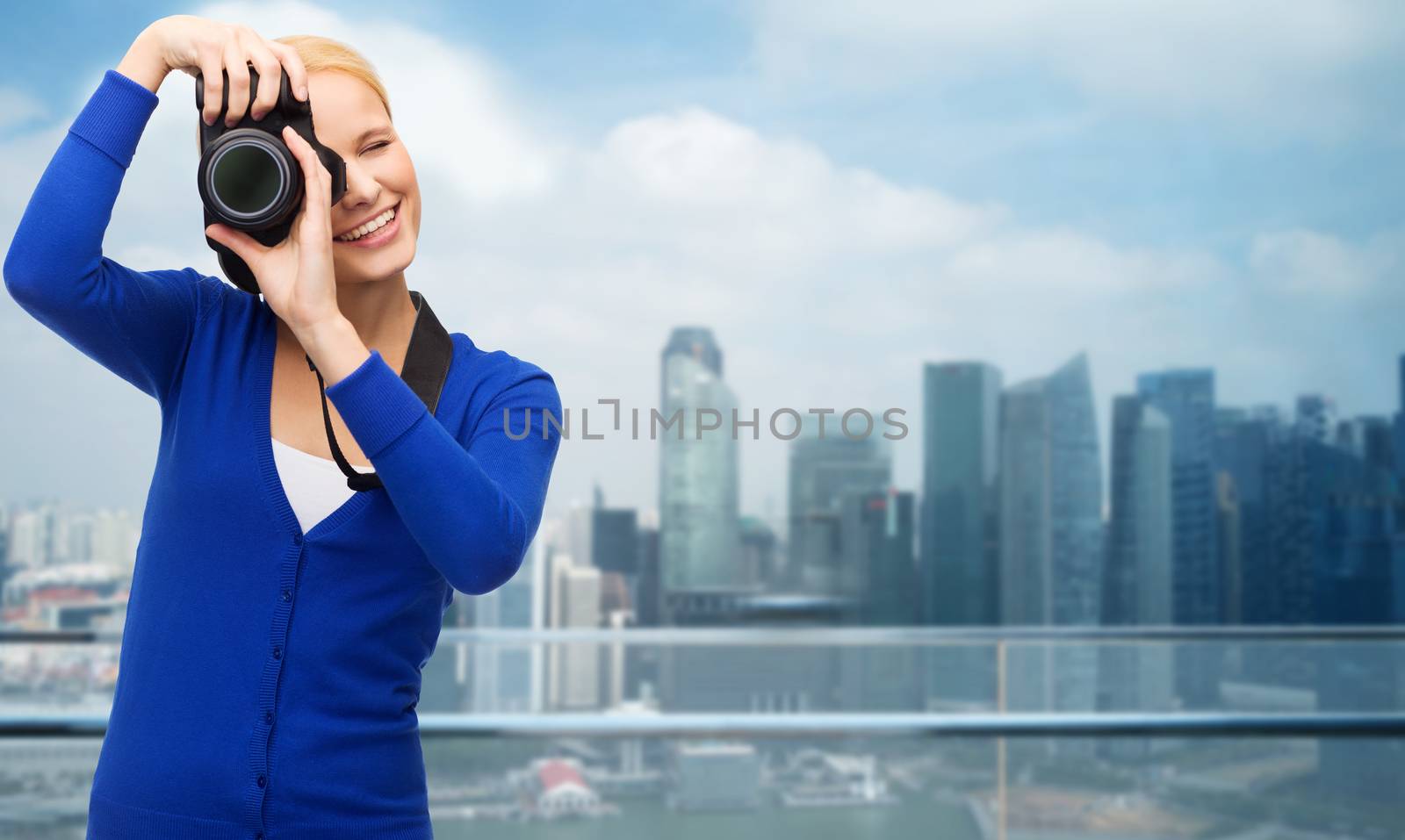 modern technology and people concept - smiling woman in casual clothes taking picture with digital camera over cityscape background