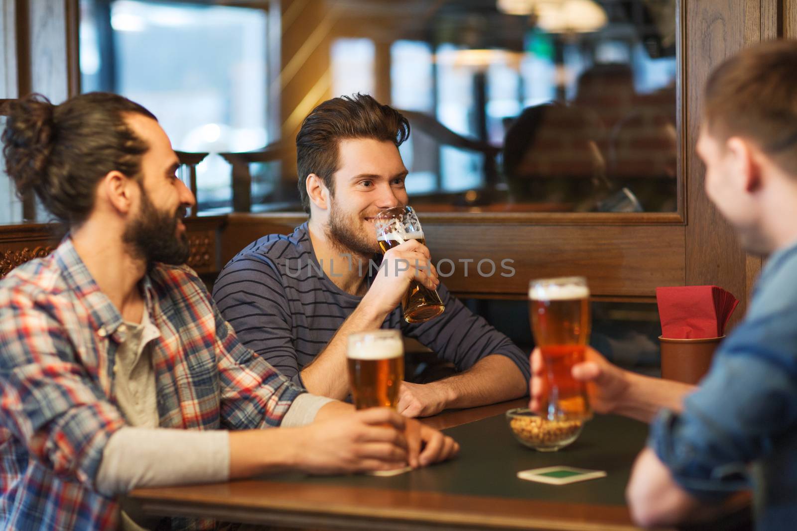 people, men, leisure, friendship and communication concept - happy male friends drinking beer at bar or pub