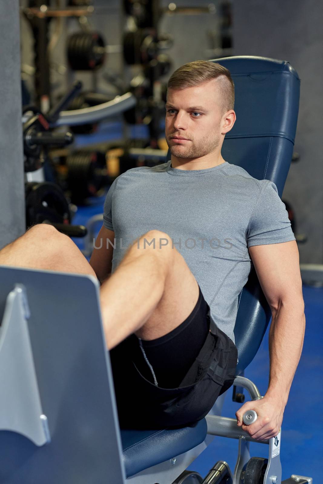 man flexing leg muscles on gym machine by dolgachov