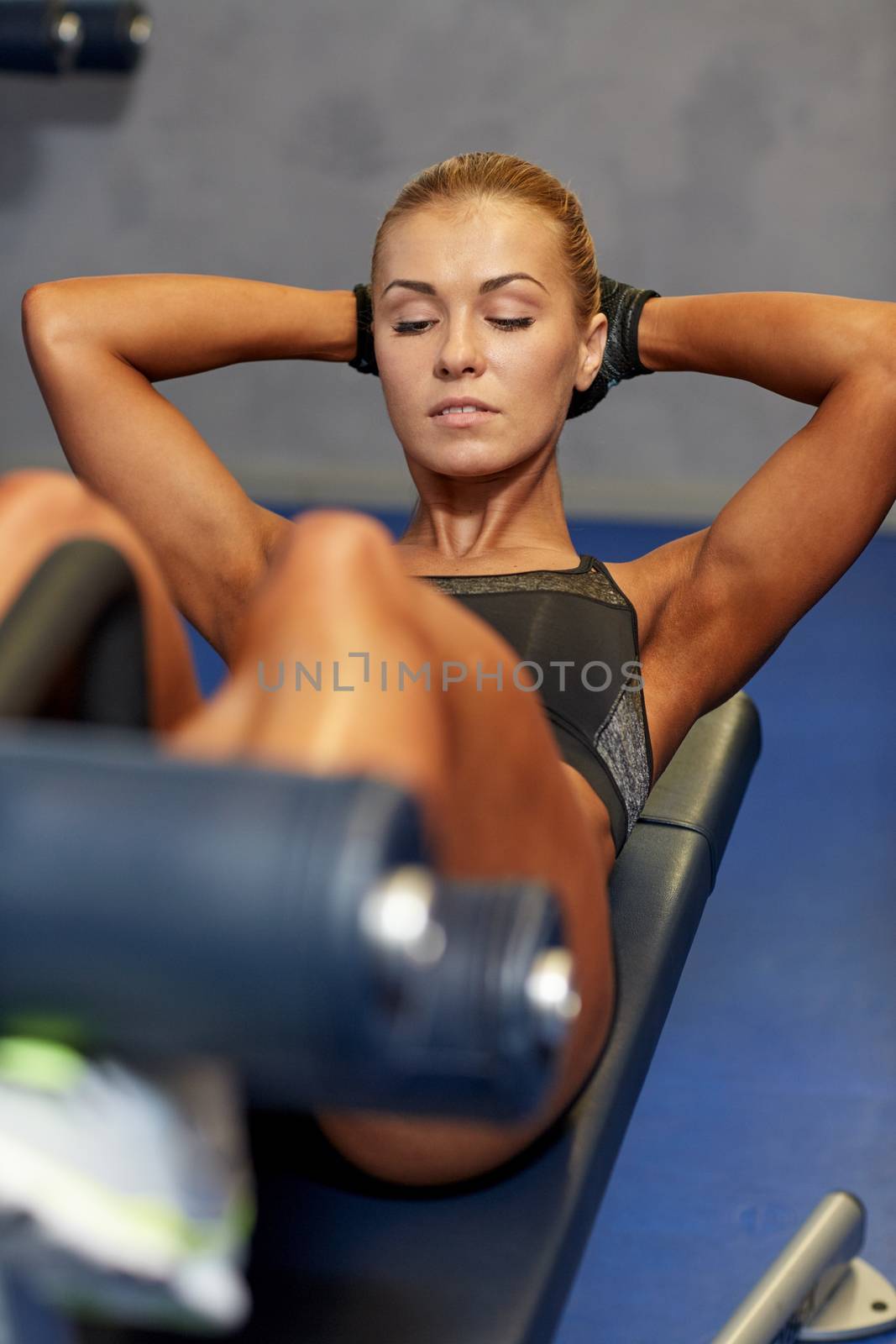 woman flexing abdominal muscles on bench in gym by dolgachov
