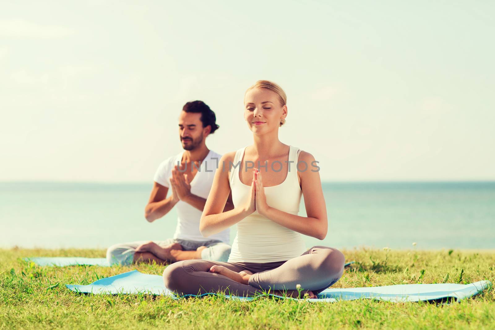 smiling couple making yoga exercises outdoors by dolgachov