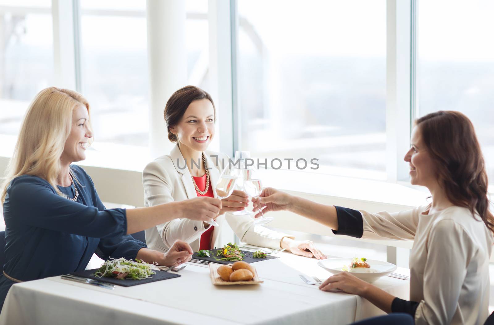 people, holidays, celebration and lifestyle concept - happy women drinking champagne and clinking glasses at restaurant