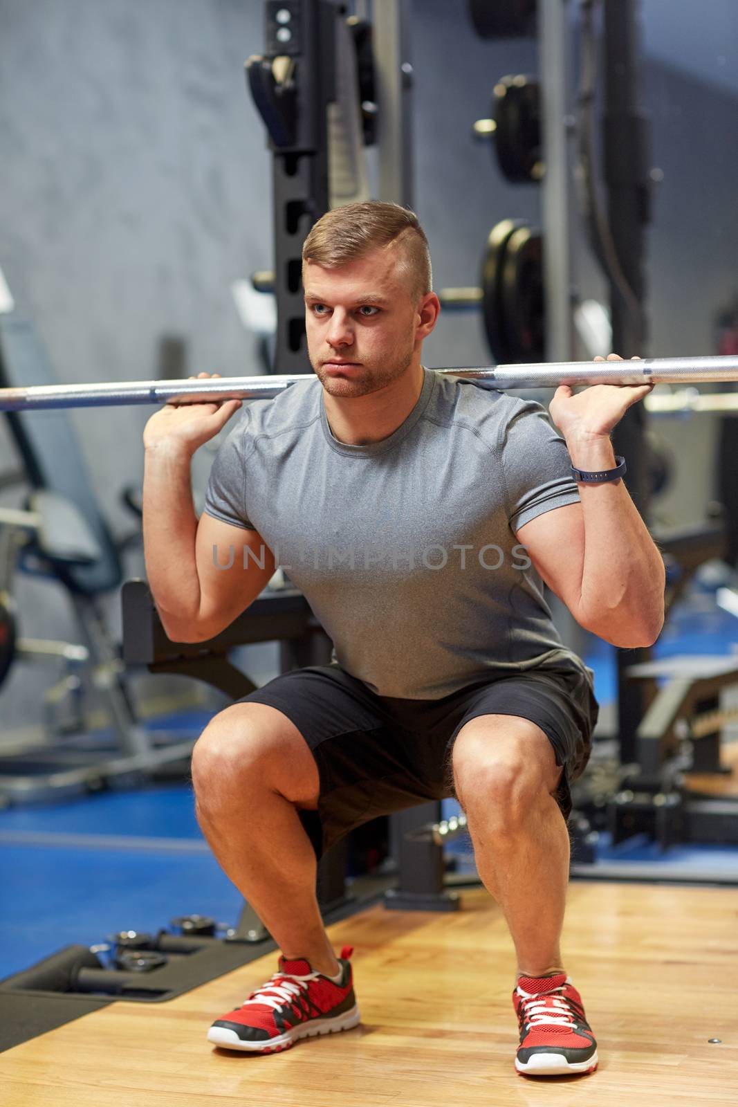 young man flexing muscles with barbell in gym by dolgachov