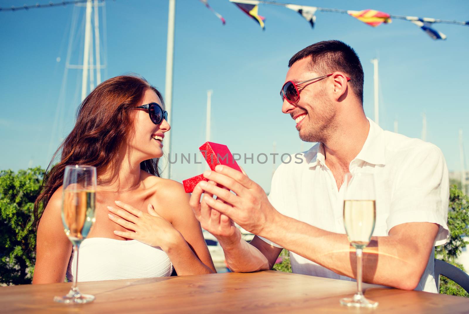 smiling couple with champagne and gift at cafe by dolgachov