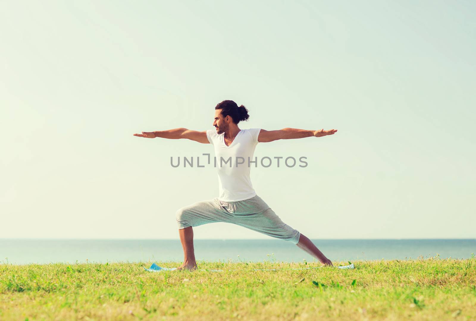 smiling man making yoga exercises outdoors by dolgachov