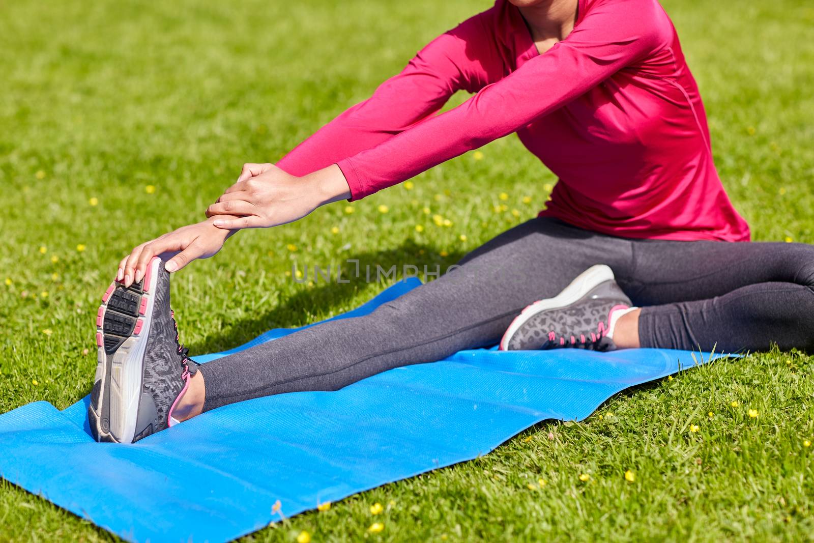 fitness, sport, training, people and lifestyle concept - close up of woman stretching leg on mat in park