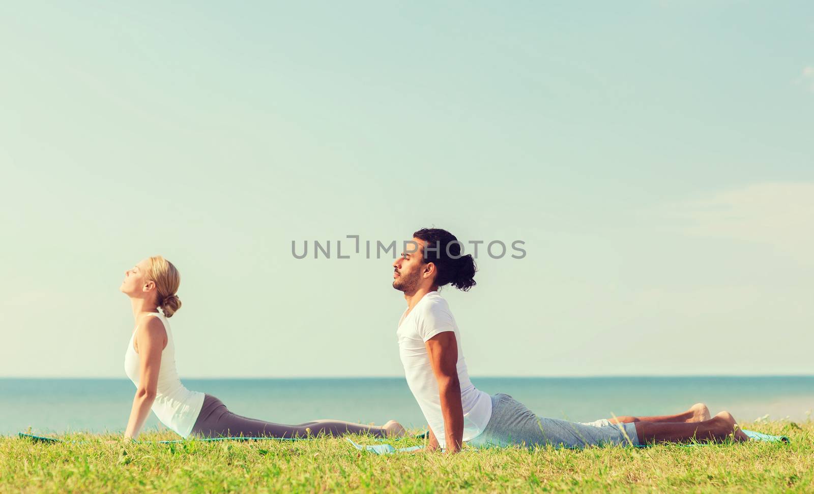 fitness, sport, friendship and lifestyle concept - smiling couple making yoga exercises lying on mats outdoors