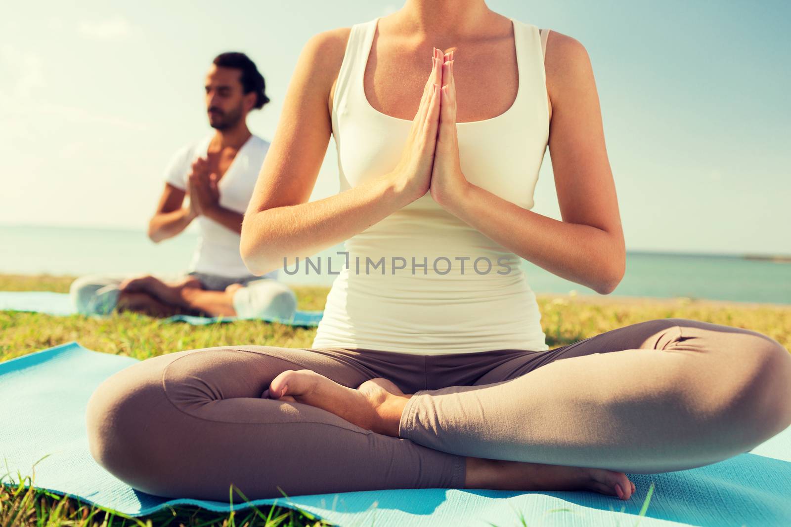 close up of couple making yoga exercises outdoors by dolgachov