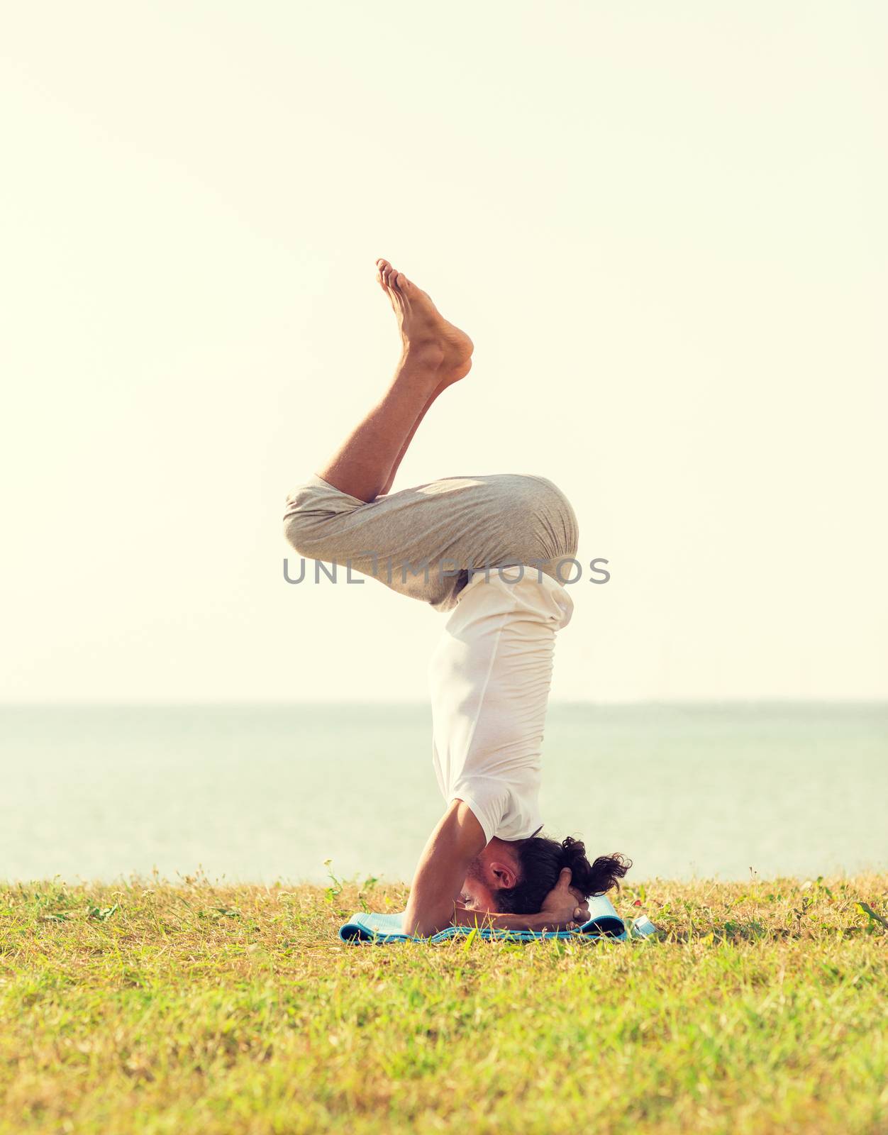 fitness, sport, people and lifestyle concept - man making yoga exercises on sand outdoors