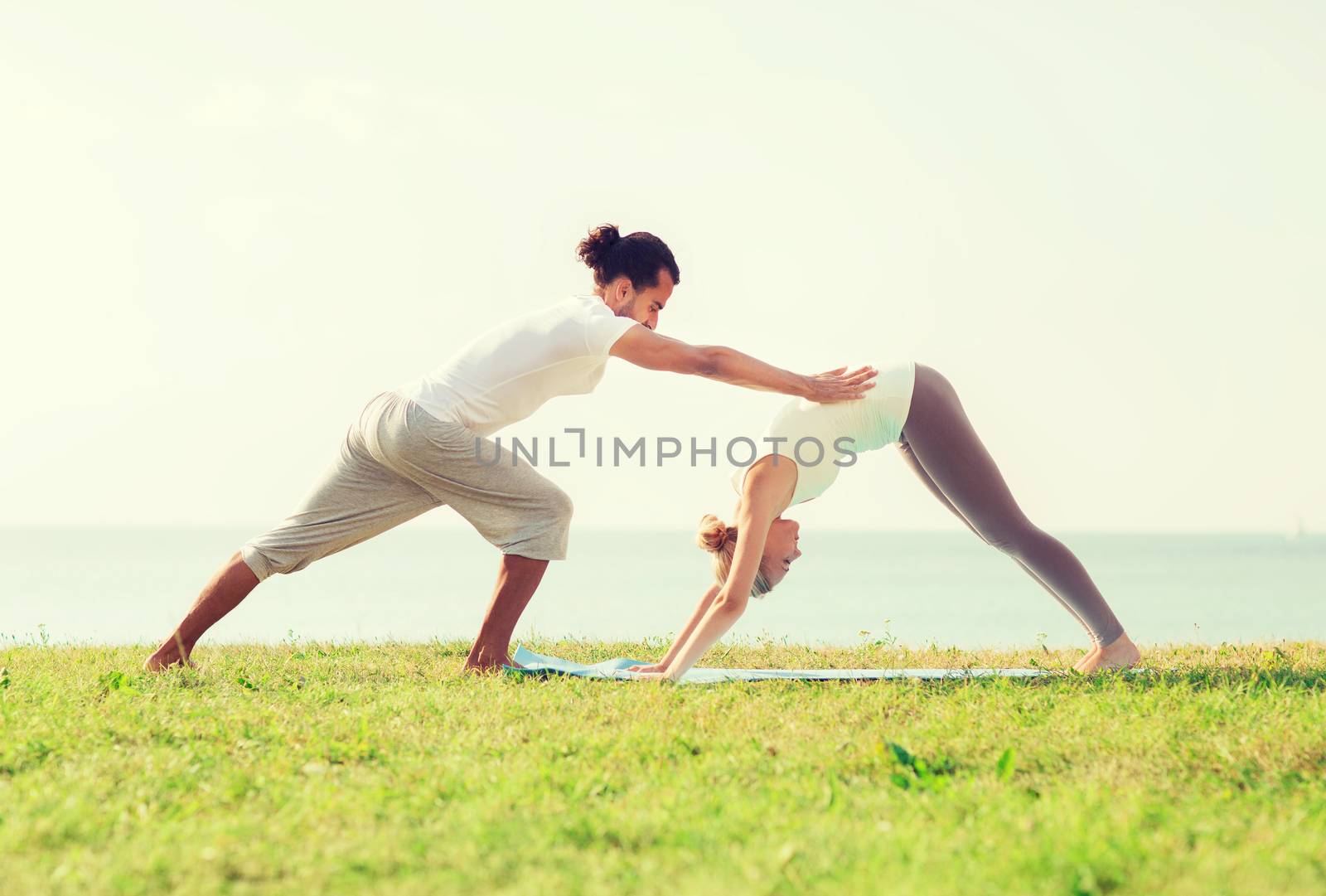 fitness, sport, friendship and lifestyle concept - smiling couple making yoga exercises on mat outdoors