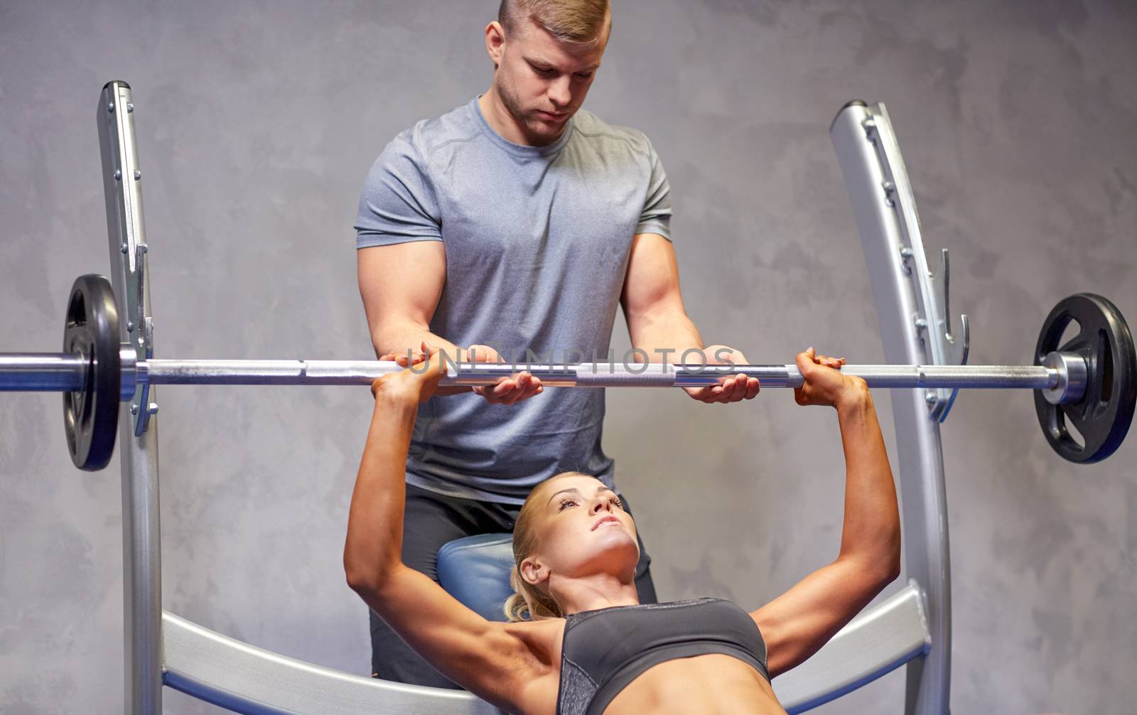 man and woman with barbell flexing muscles in gym by dolgachov