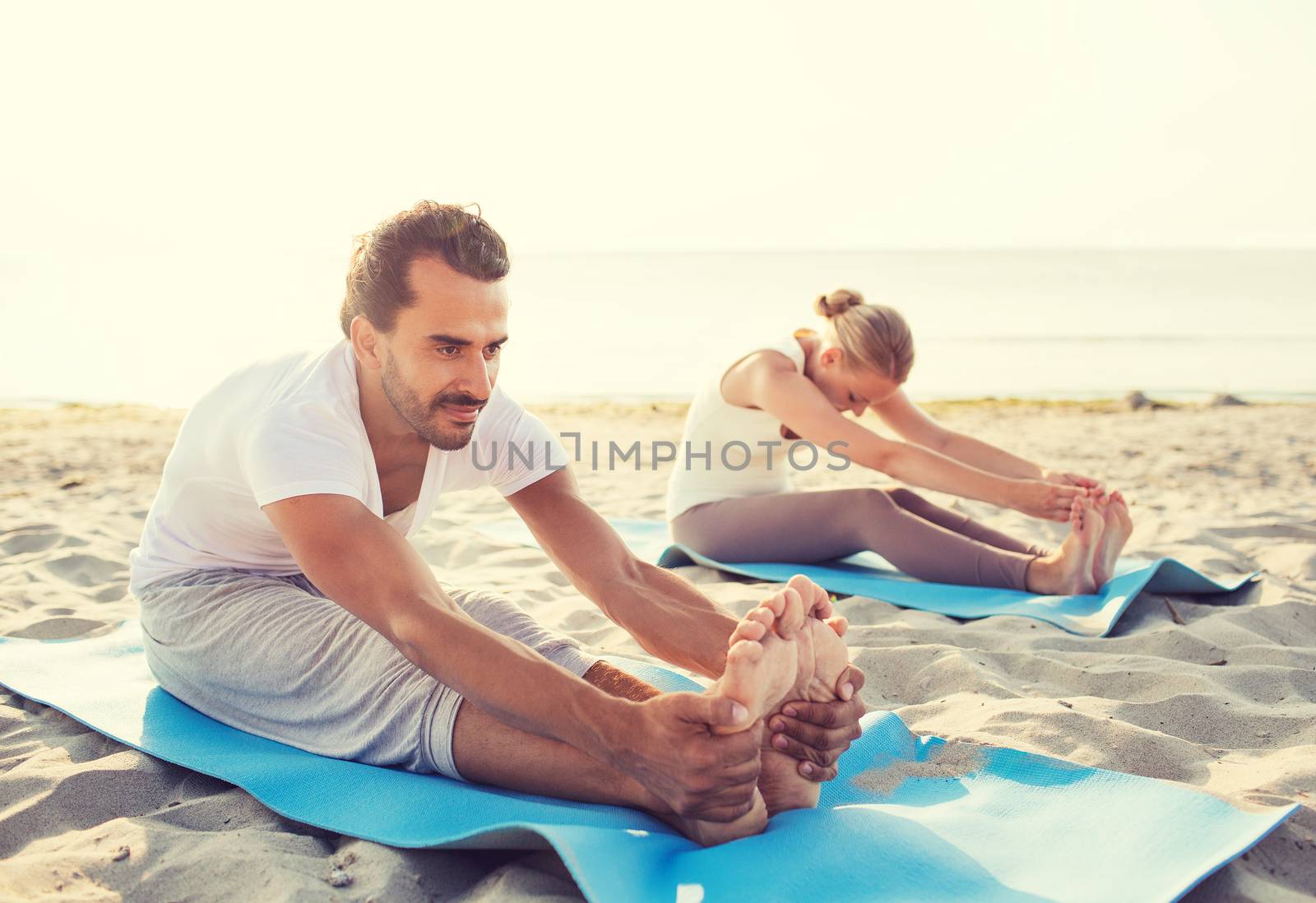 fitness, sport, friendship and lifestyle concept - couple making yoga exercises sitting on mats outdoors