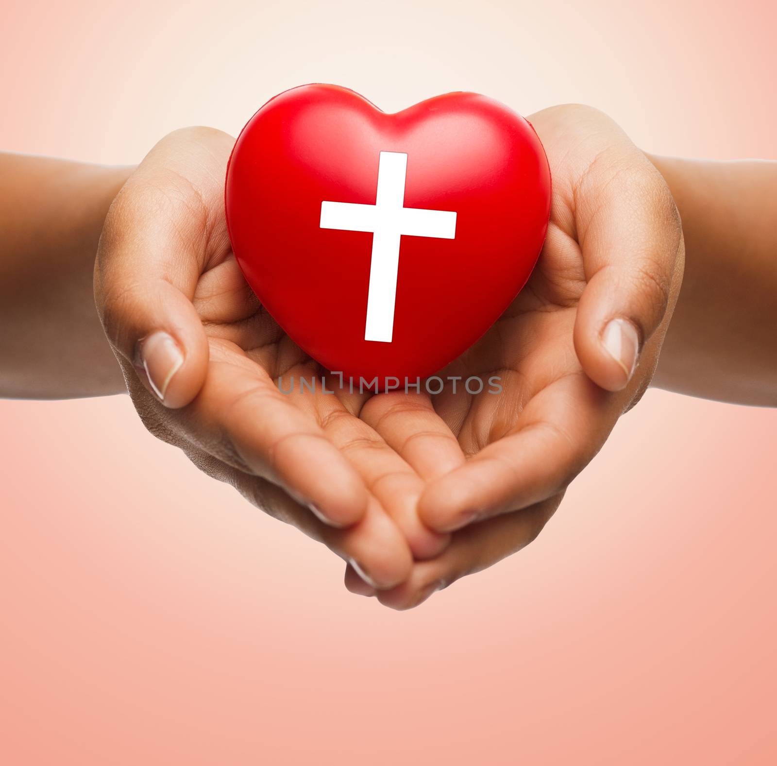 religion, christianity and charity concept - close up of female hands holding red heart with christian cross symbol over beige background