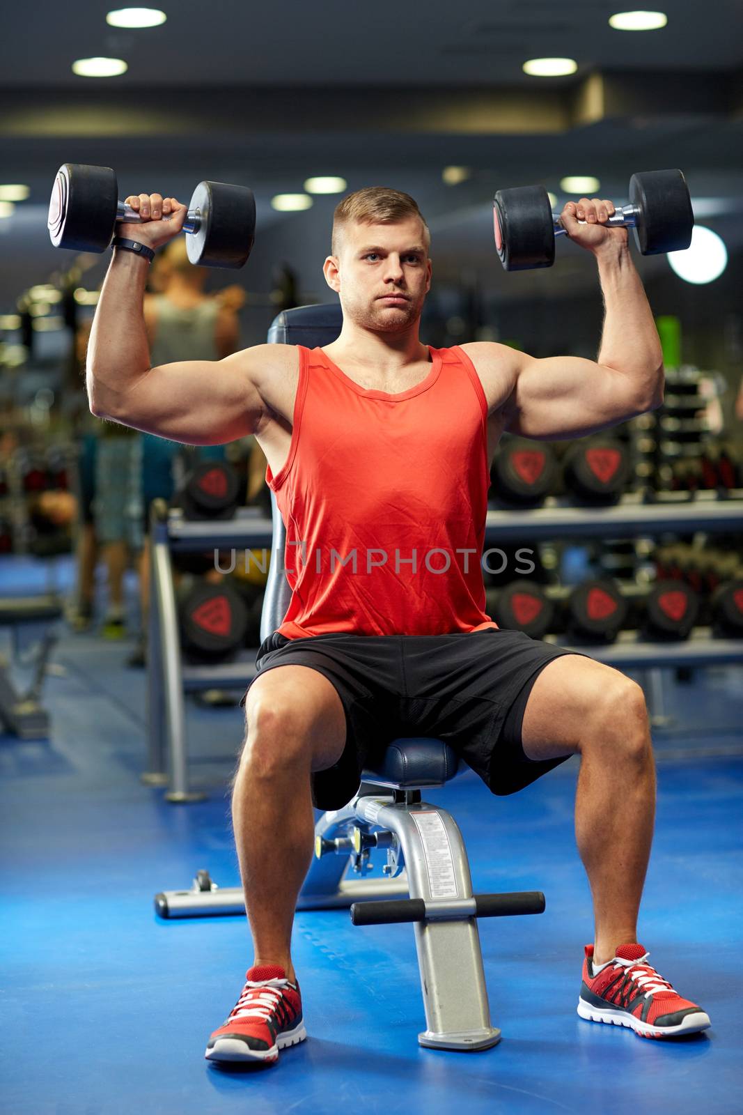 young man with dumbbells flexing muscles in gym by dolgachov