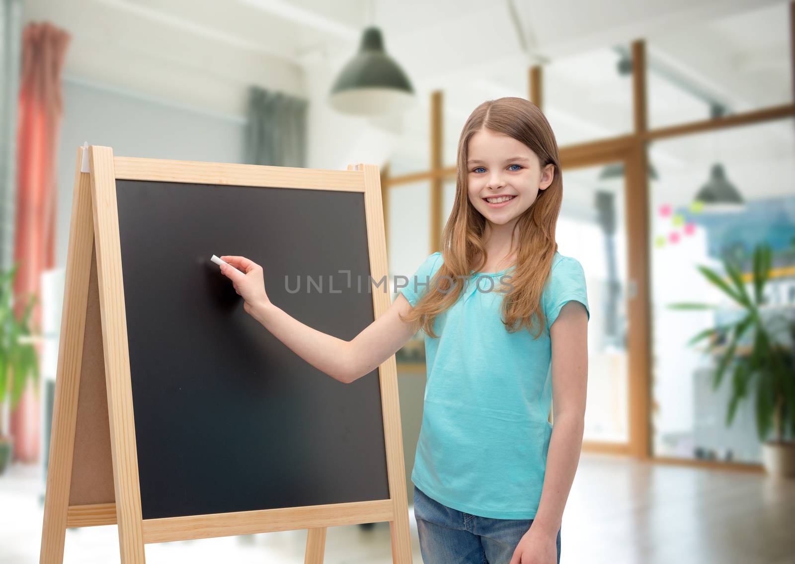 people, children, advertisement and education concept - happy little girl with blackboard and chalk over school class room background