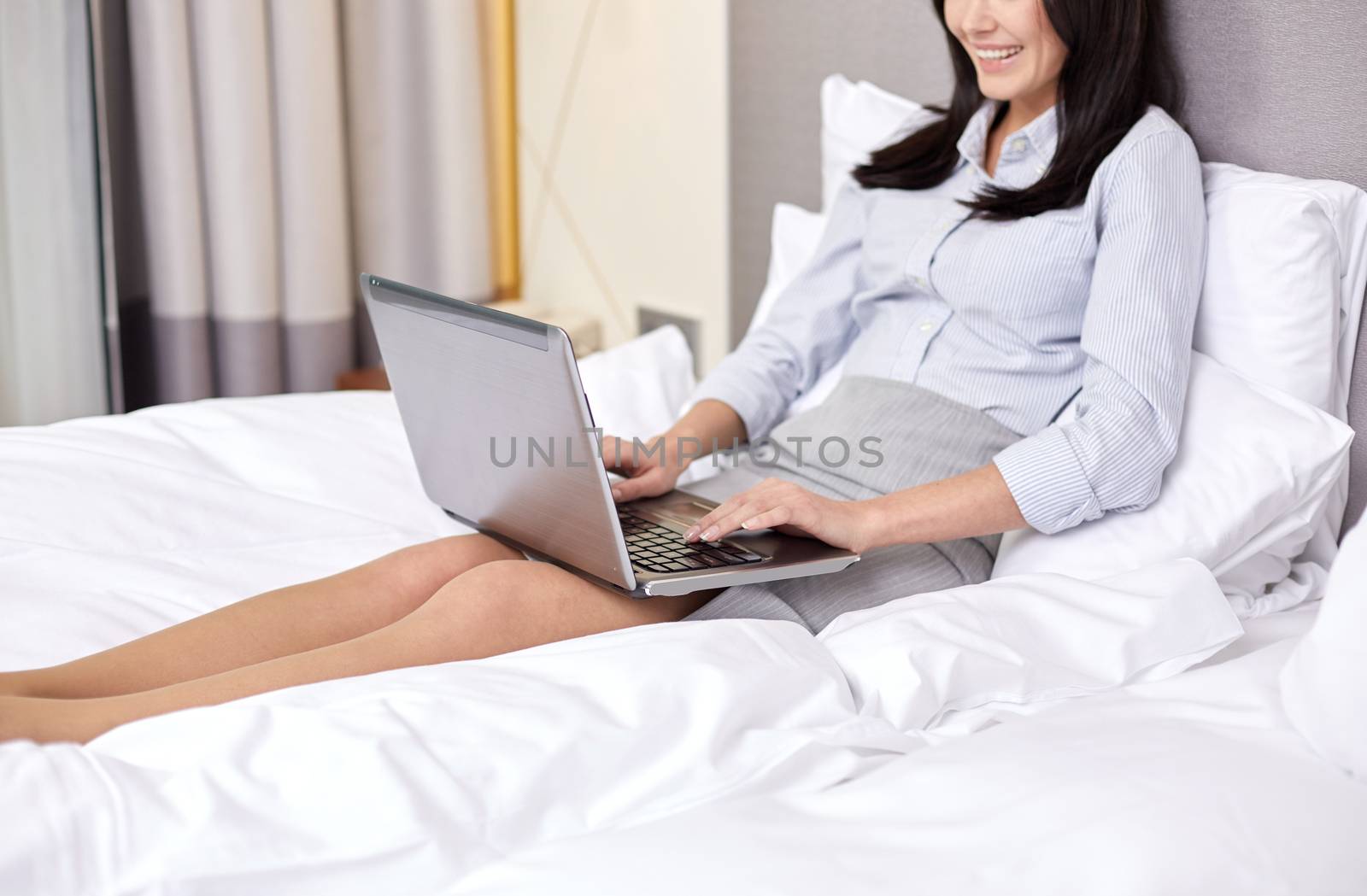 smiling businesswoman with laptop typing in bed by dolgachov