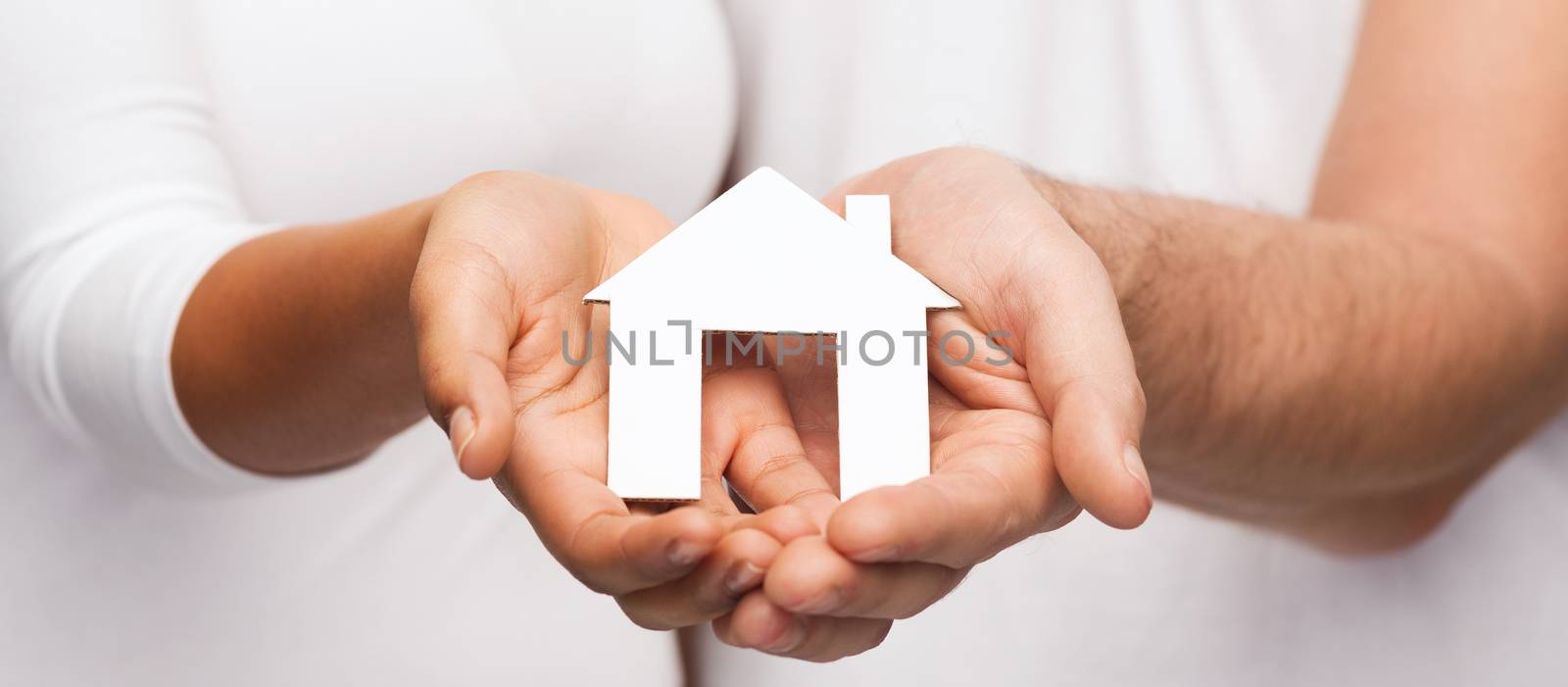 real estate and family concept - closeup of couple hands holding paper house