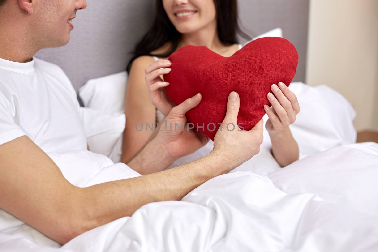 smiling couple in bed with red heart shape pillow by dolgachov