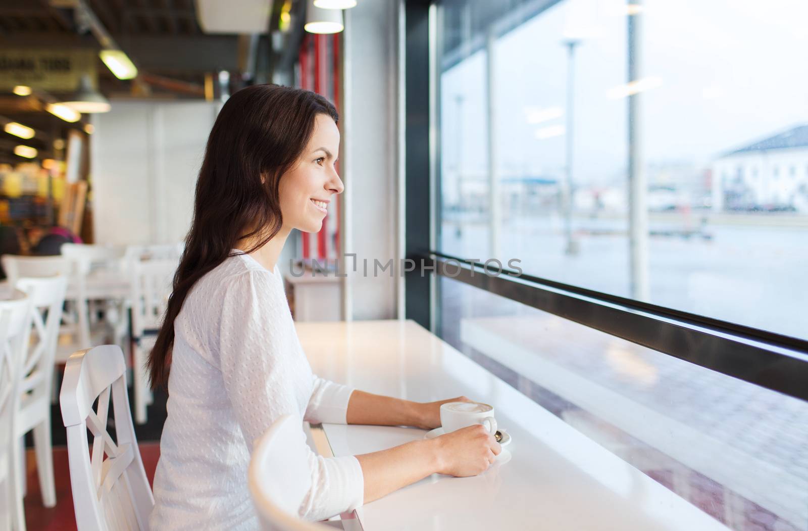 leisure, drinks, people and lifestyle concept - smiling young woman drinking coffee at cafe