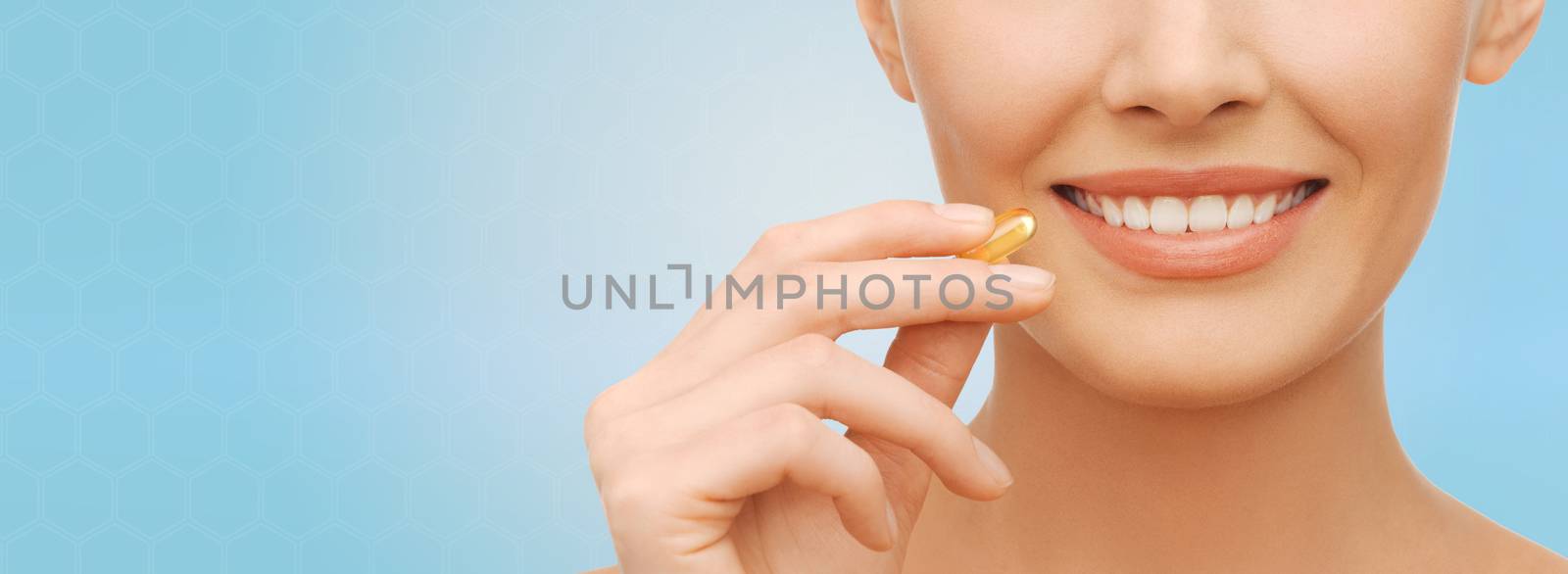 healthcare, people and beauty concept - beautiful woman face and hand holding omega 3 vitamins capsule over blue background