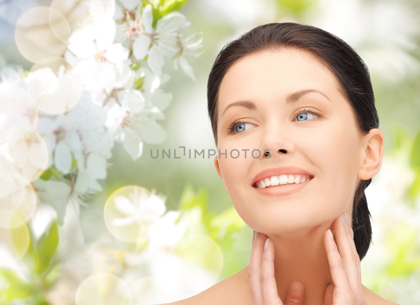 beauty, people and health concept - beautiful young woman touching her face and neck over green blooming garden background