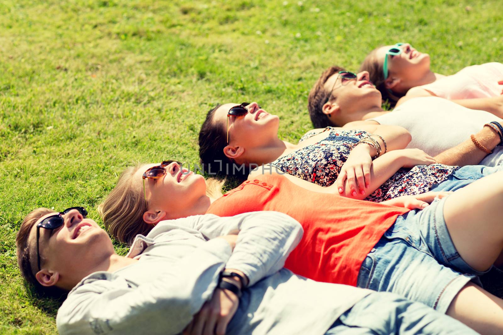 friendship, leisure, summer and people concept - group of smiling friends lying on grass outdoors