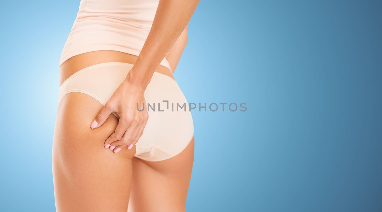 people, health, body care and beauty concept - close up of woman in underwear touching buttock over blue background