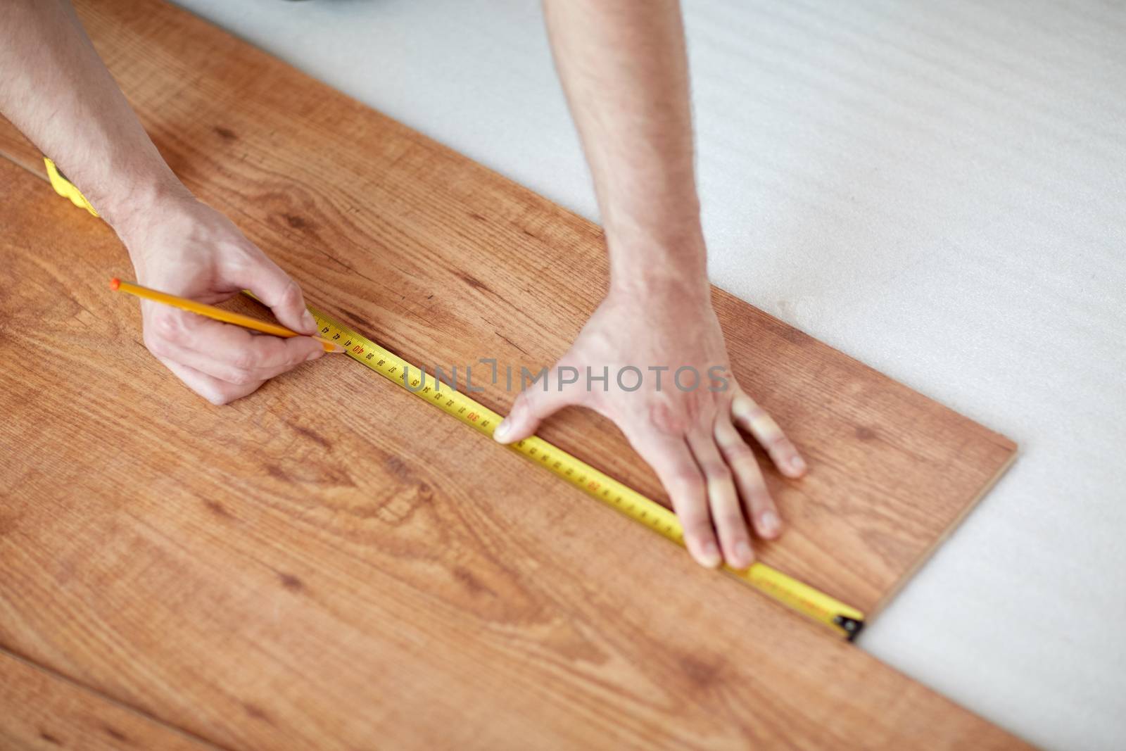 repair, building, floor and people concept - close up of male hands measuring wooden flooring with ruler and making mark by pencil