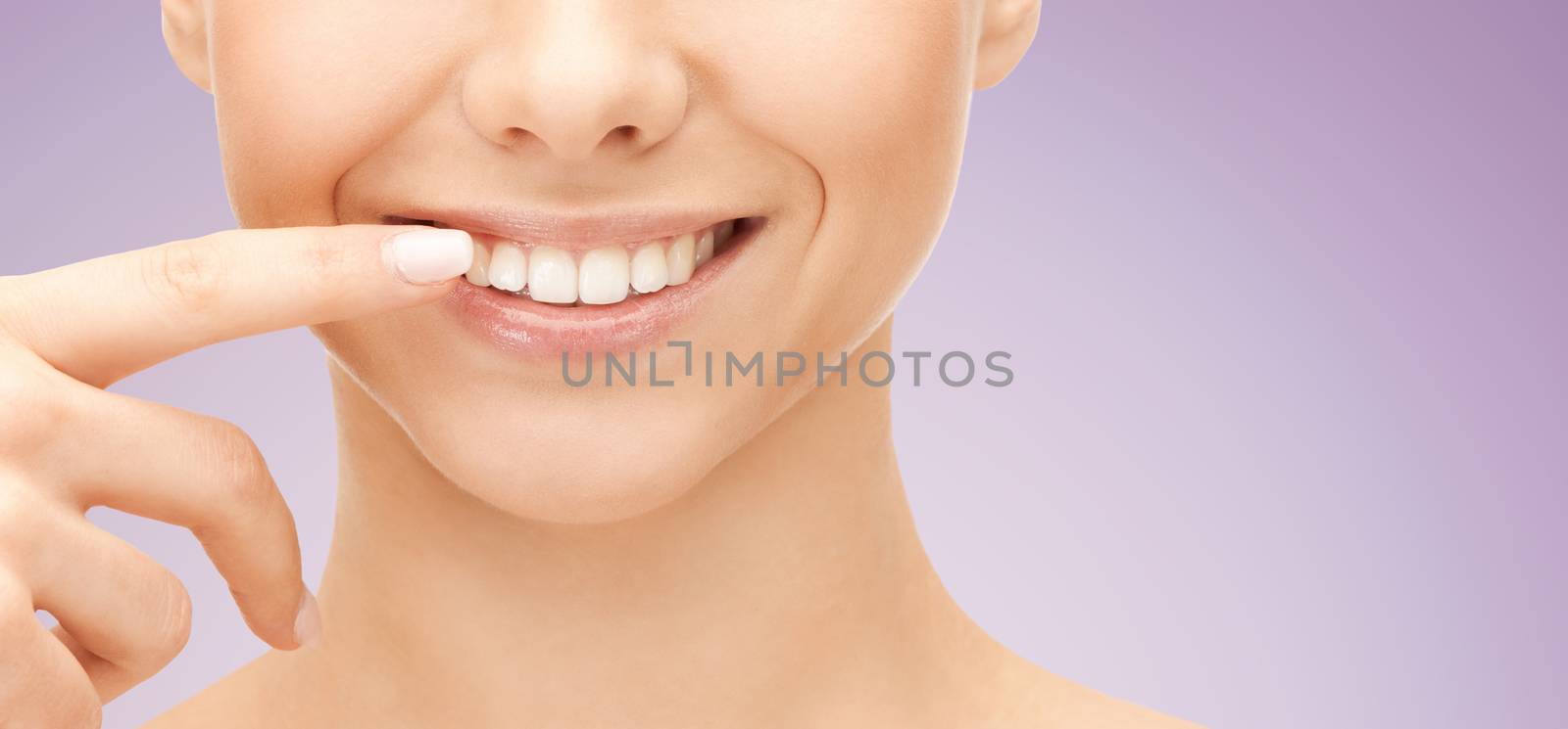 dental health, beauty, hygiene and people concept - close up of smiling woman face pointing to teeth over violet background