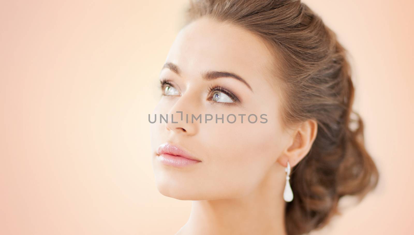 people, beauty, jewelry and accessories concept - beautiful woman with diamond earrings over beige background