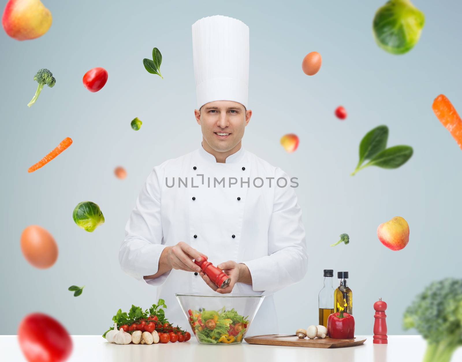 profession, vegetarian, food and people concept - happy male chef cooking and seasoning vegetable salad over gray background