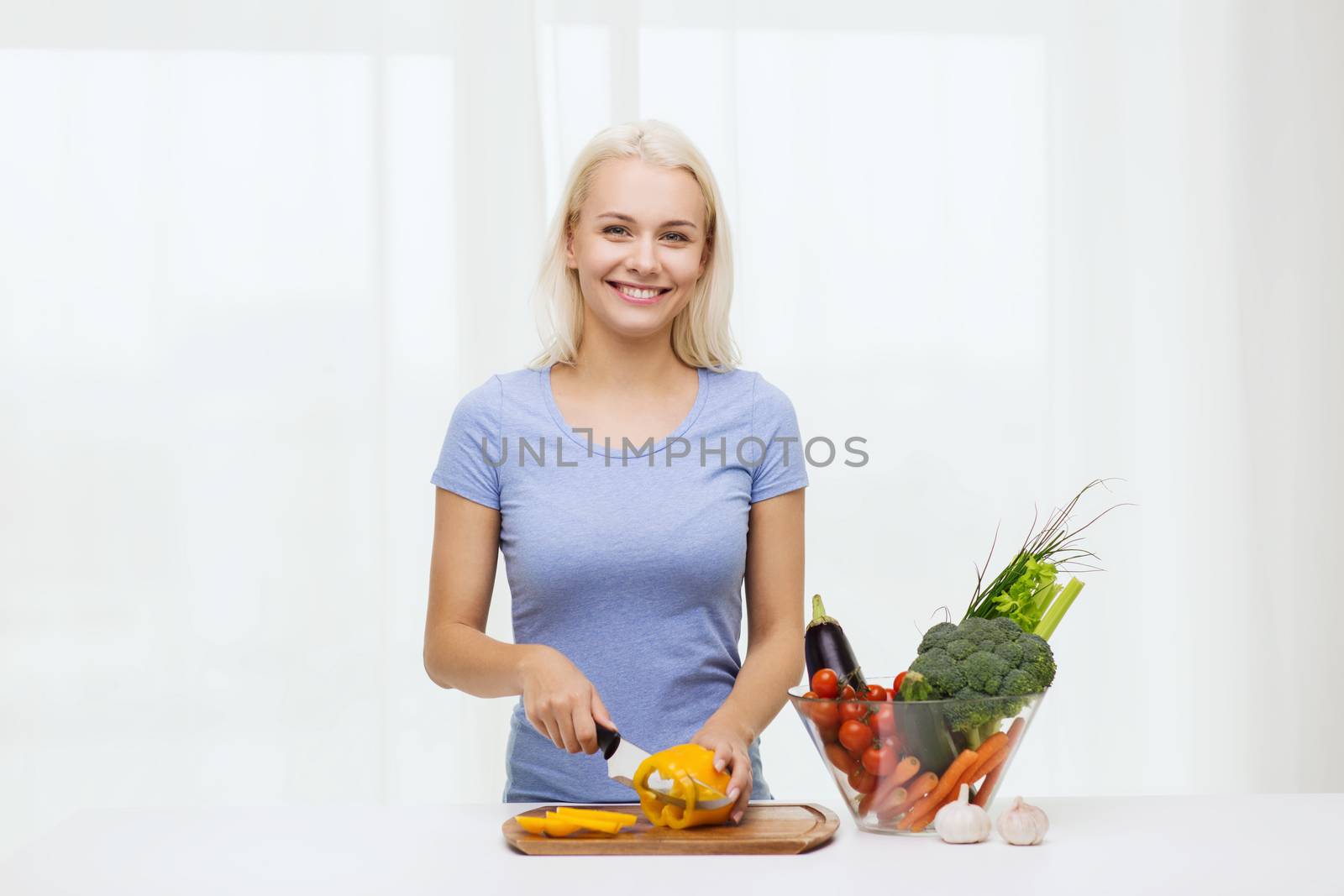 smiling young woman chopping vegetables at home by dolgachov