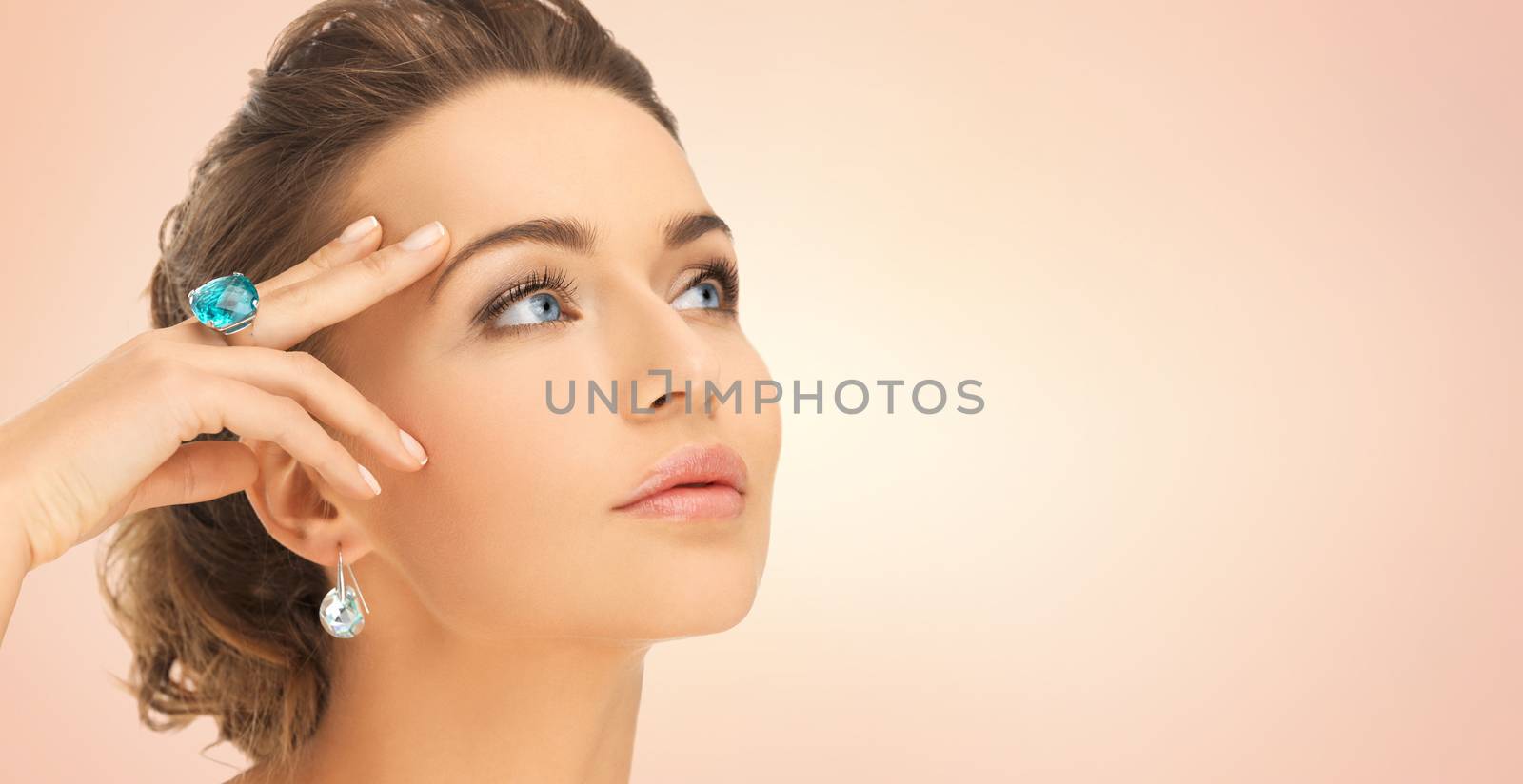 beauty, jewelry, people and accessories concept - close up of woman face with cocktail ring on hand and earrings over beige background