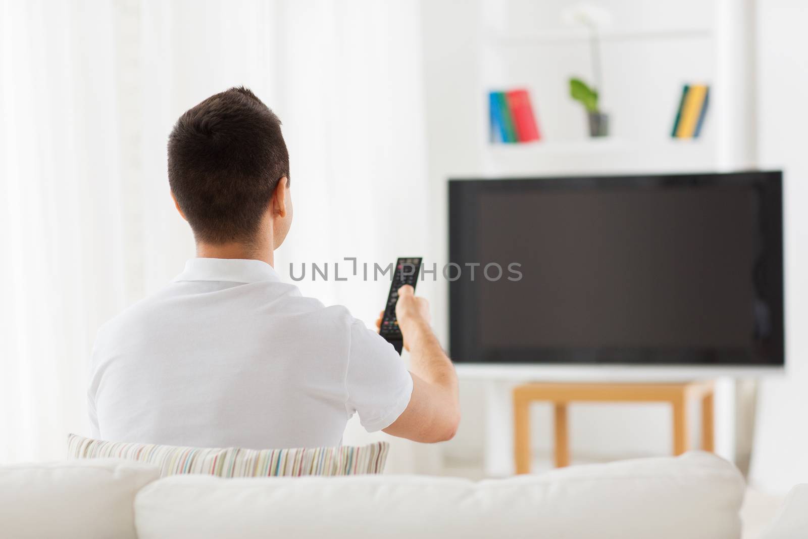 leisure, technology, mass media and people concept - man watching tv and changing channels at home from back