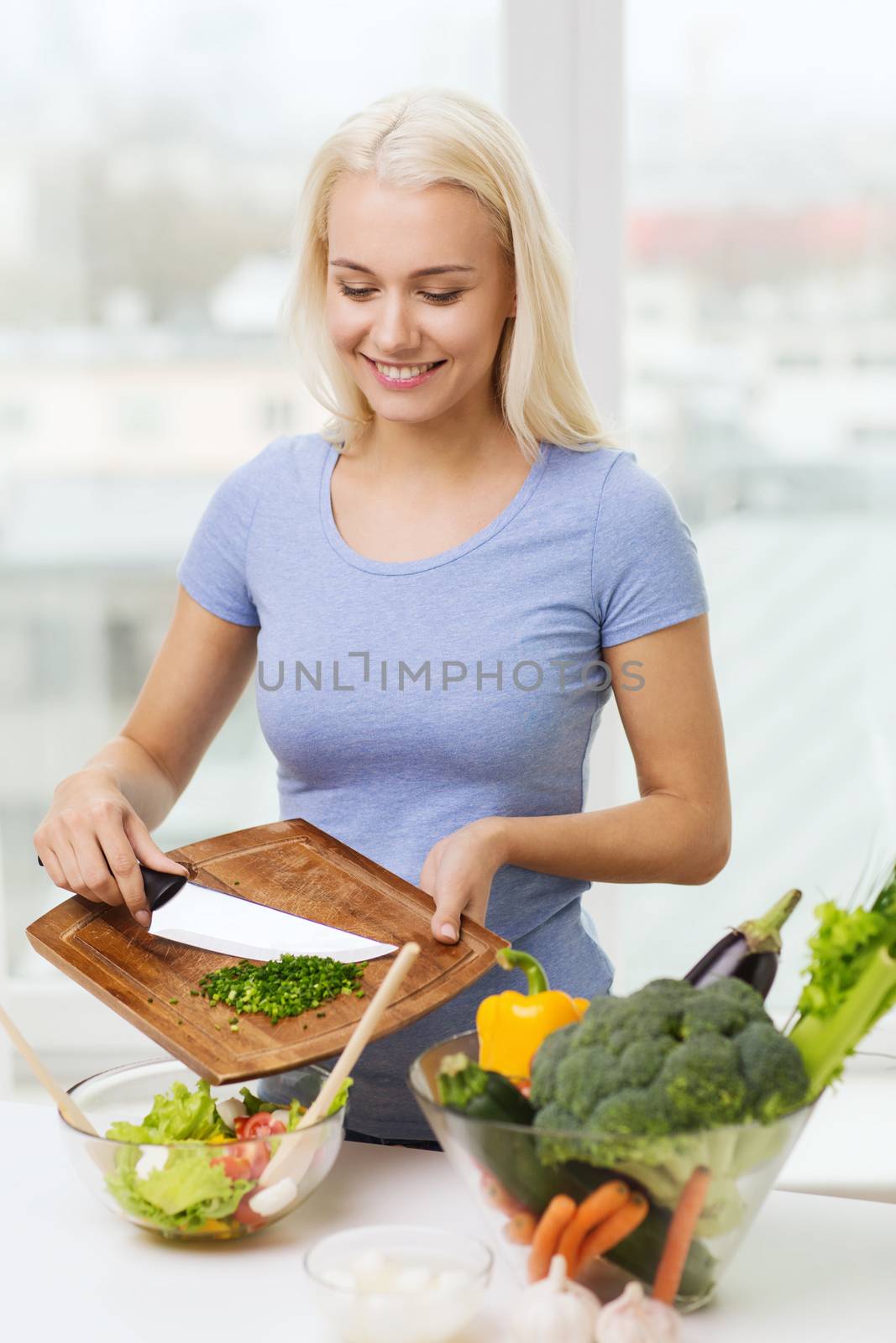 smiling woman cooking vegetable salad at home by dolgachov