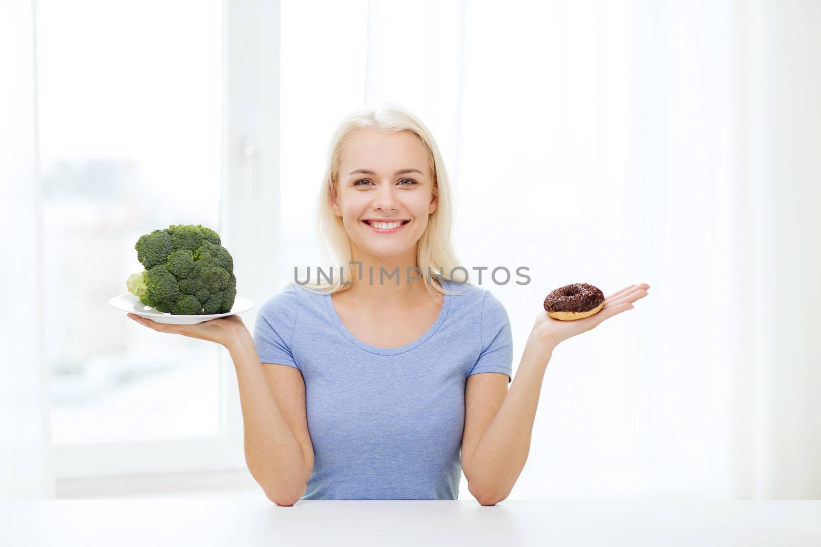 smiling woman with broccoli and donut at home by dolgachov