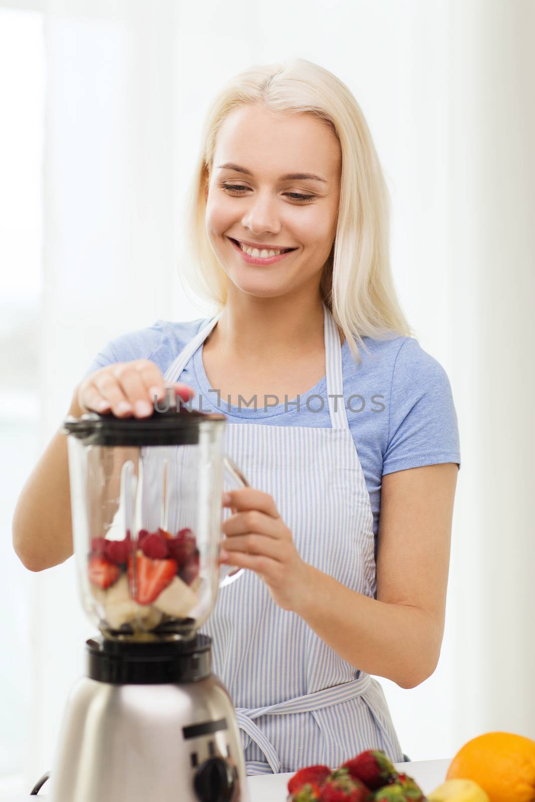 smiling woman with blender preparing shake at home by dolgachov