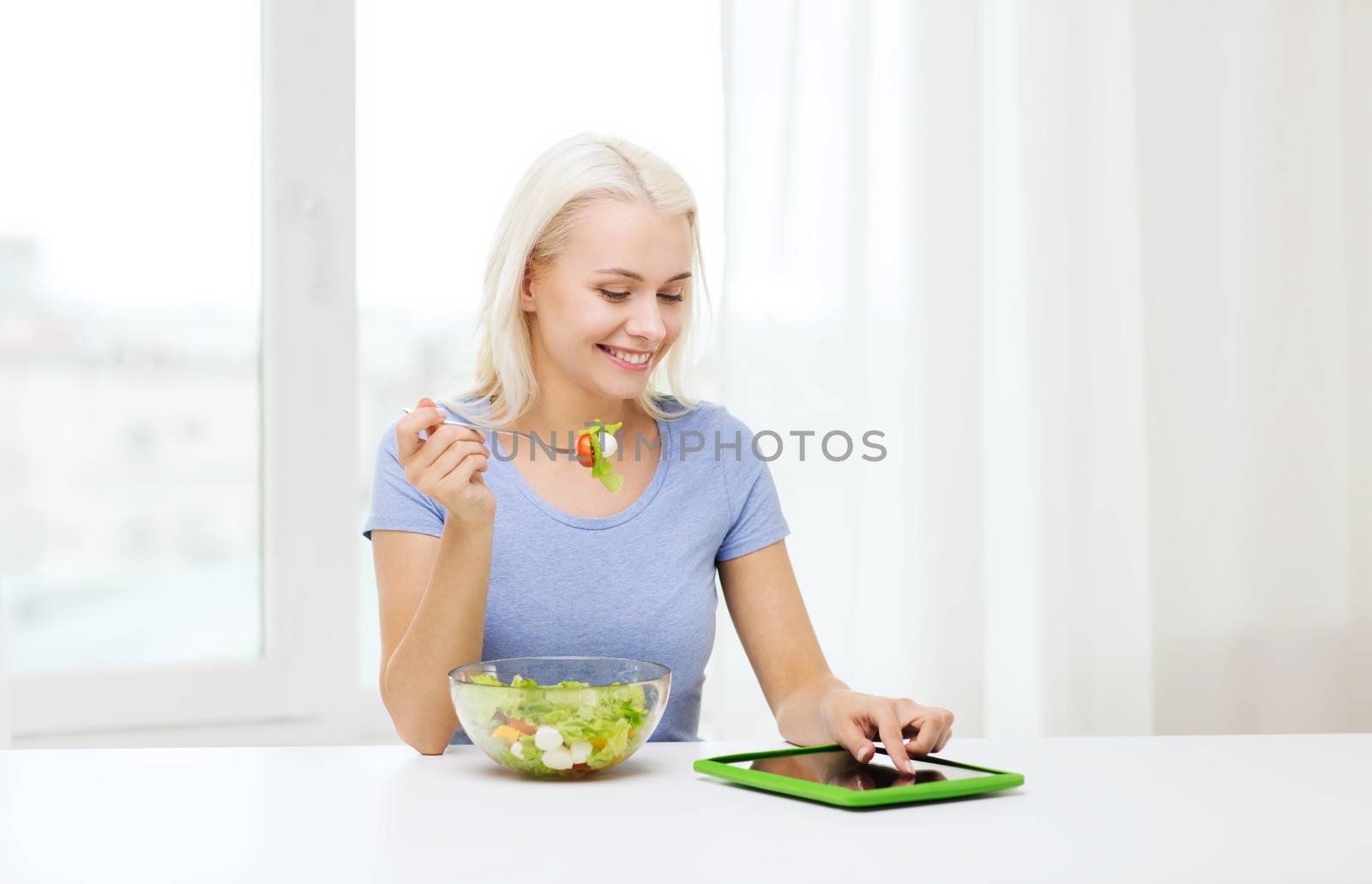 smiling woman eating salad with tablet pc at home by dolgachov