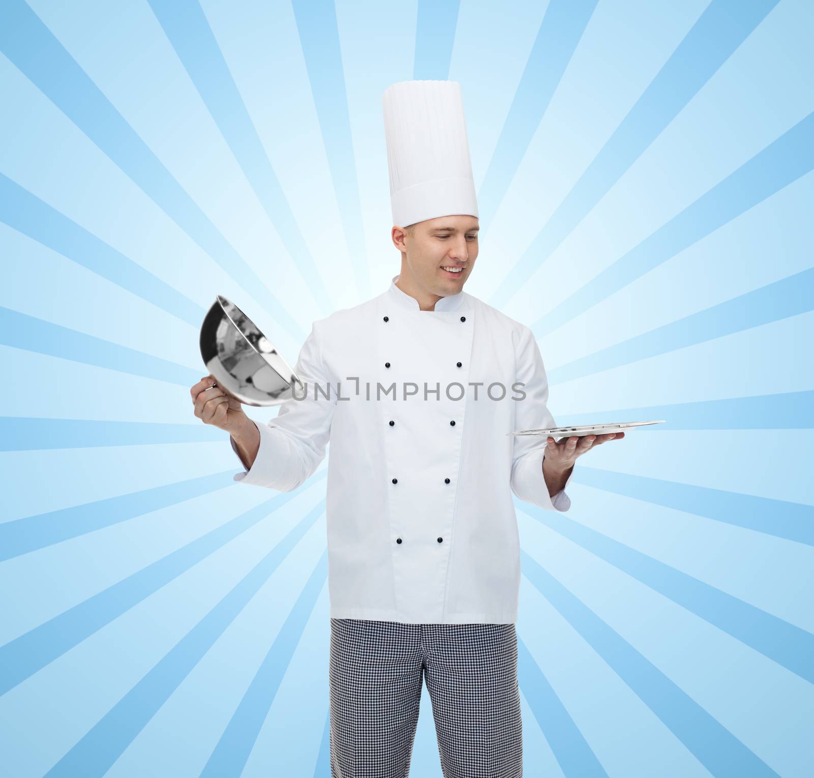 cooking, profession and people concept - happy male chef cook opening cloche cover over blue burst rays background