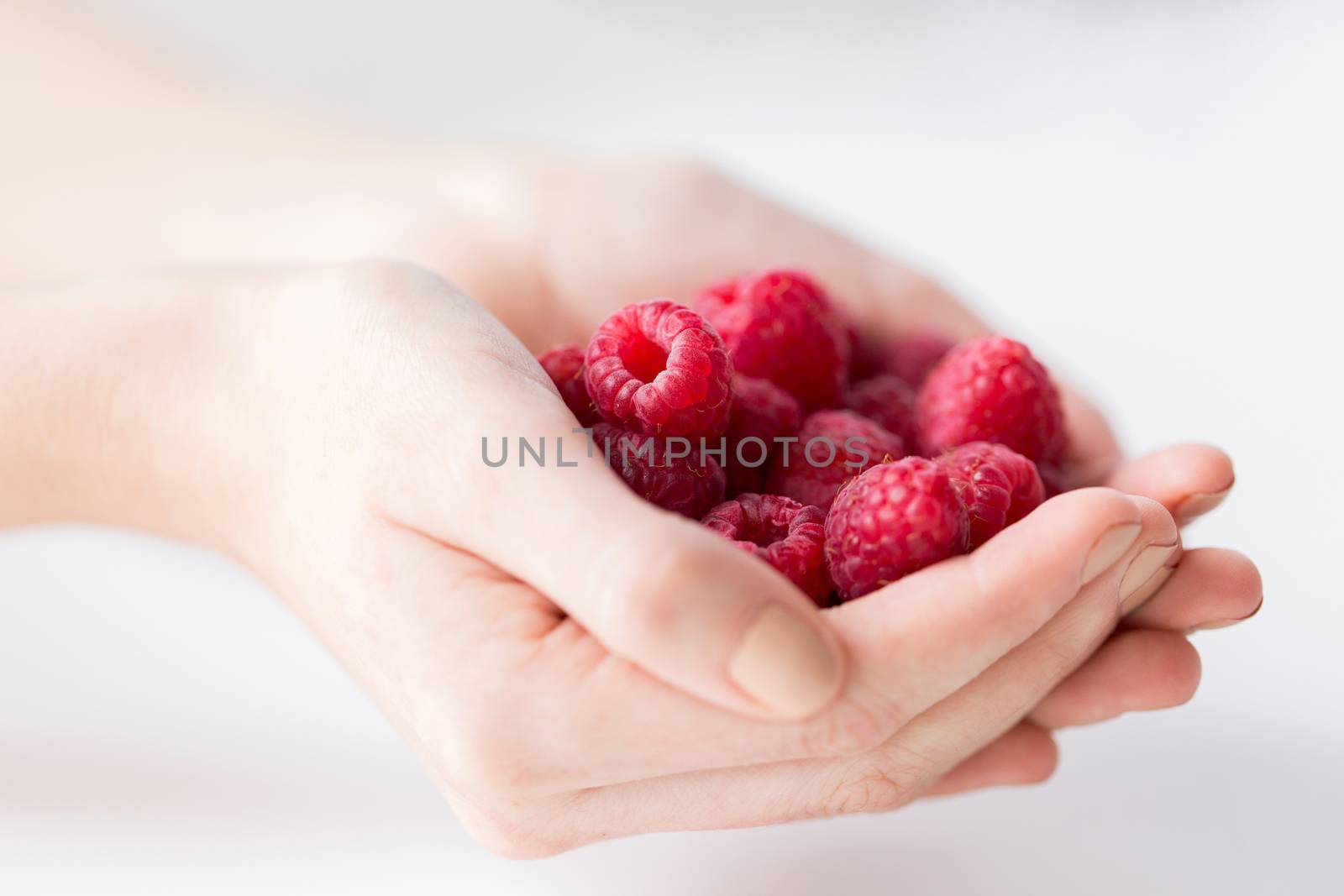 healthy eating, dieting, vegetarian food and people concept - close up of woman hands holding raspberries at home