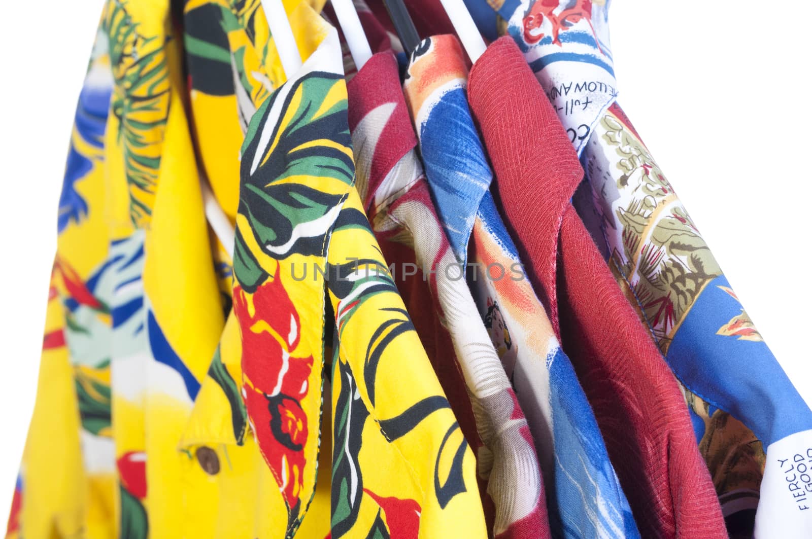 Selection of five colorful yellow, red, blue and green Hawaiian shirts arranged on hangers on white background