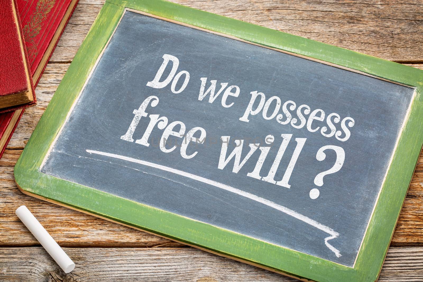 Do we possess free? A question in  white chalk on a vintage blackboard with a stack of books against rustic wooden table