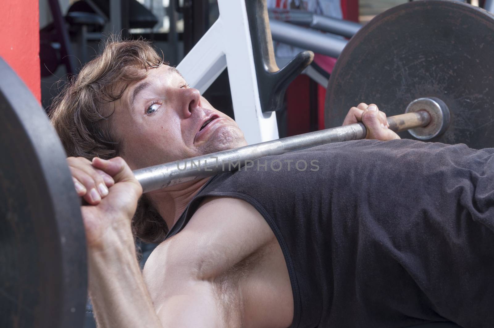 Caucasian man working out in gym is stuck under heavy barbell on bench press