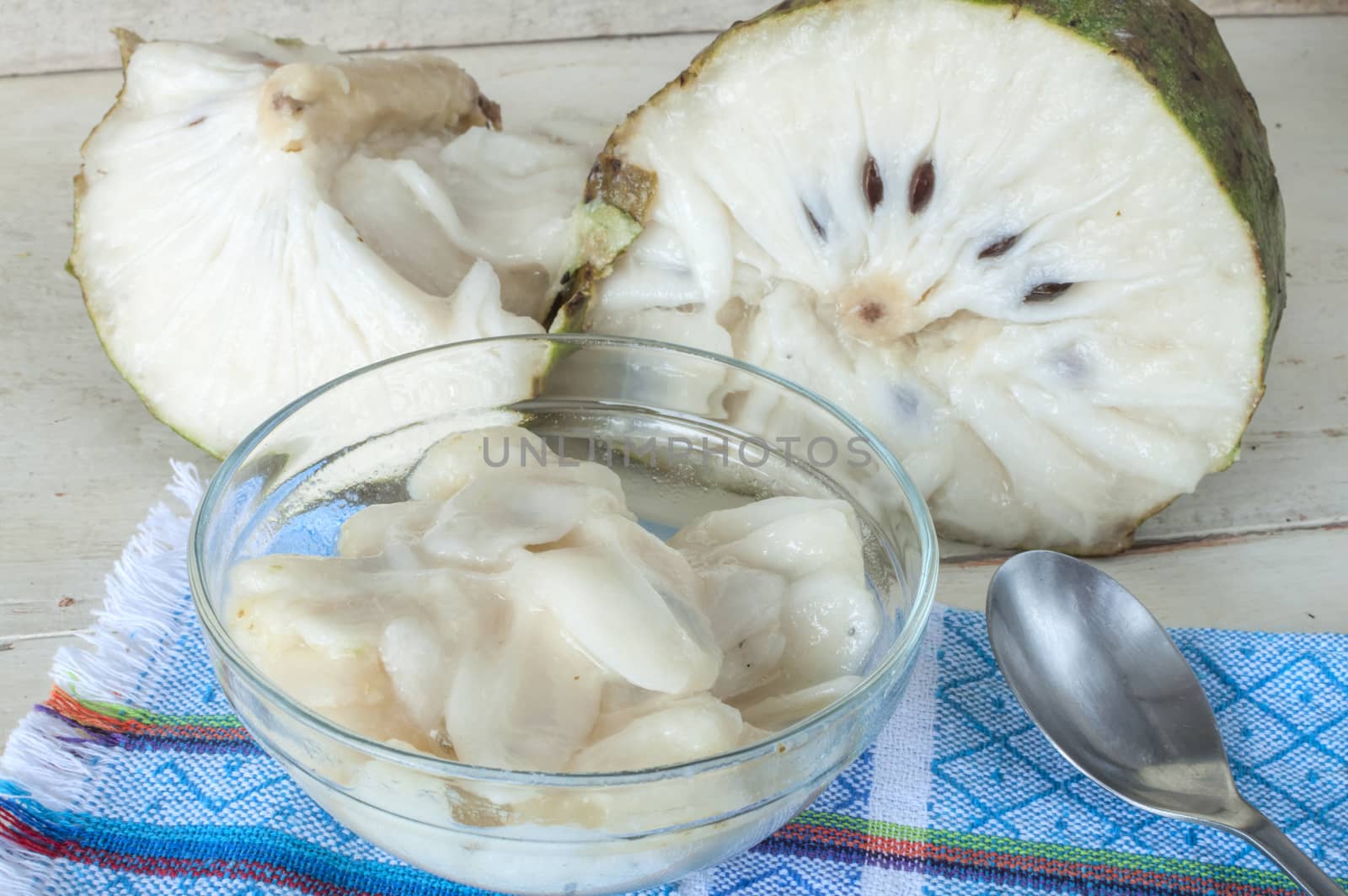 Bowl of white flesh of soursop fruit in front of whole cut fruit on rustic wooden white table
