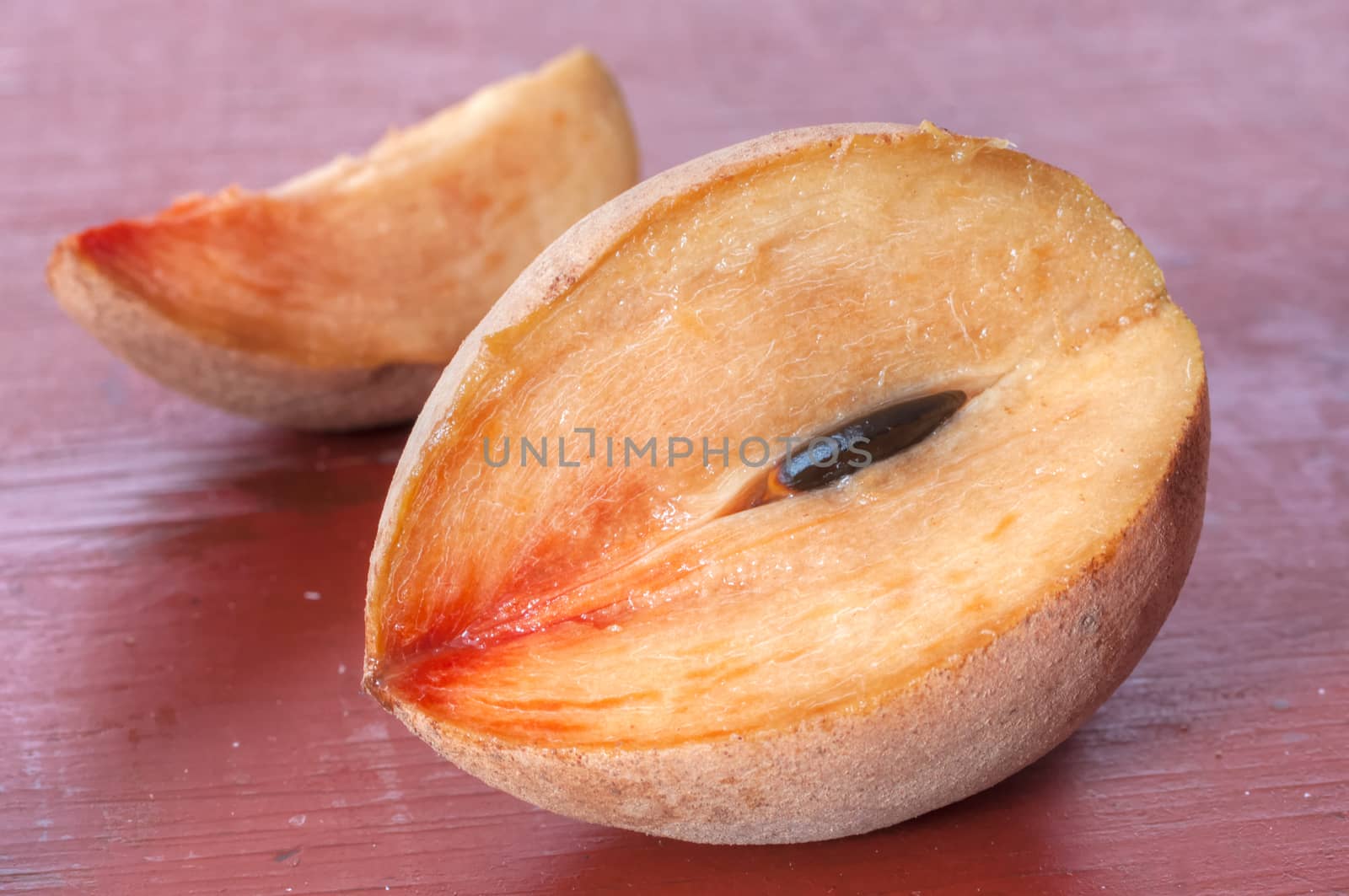 Closeup of ripe cut sapodilla chicozapote fruit and slice on red table