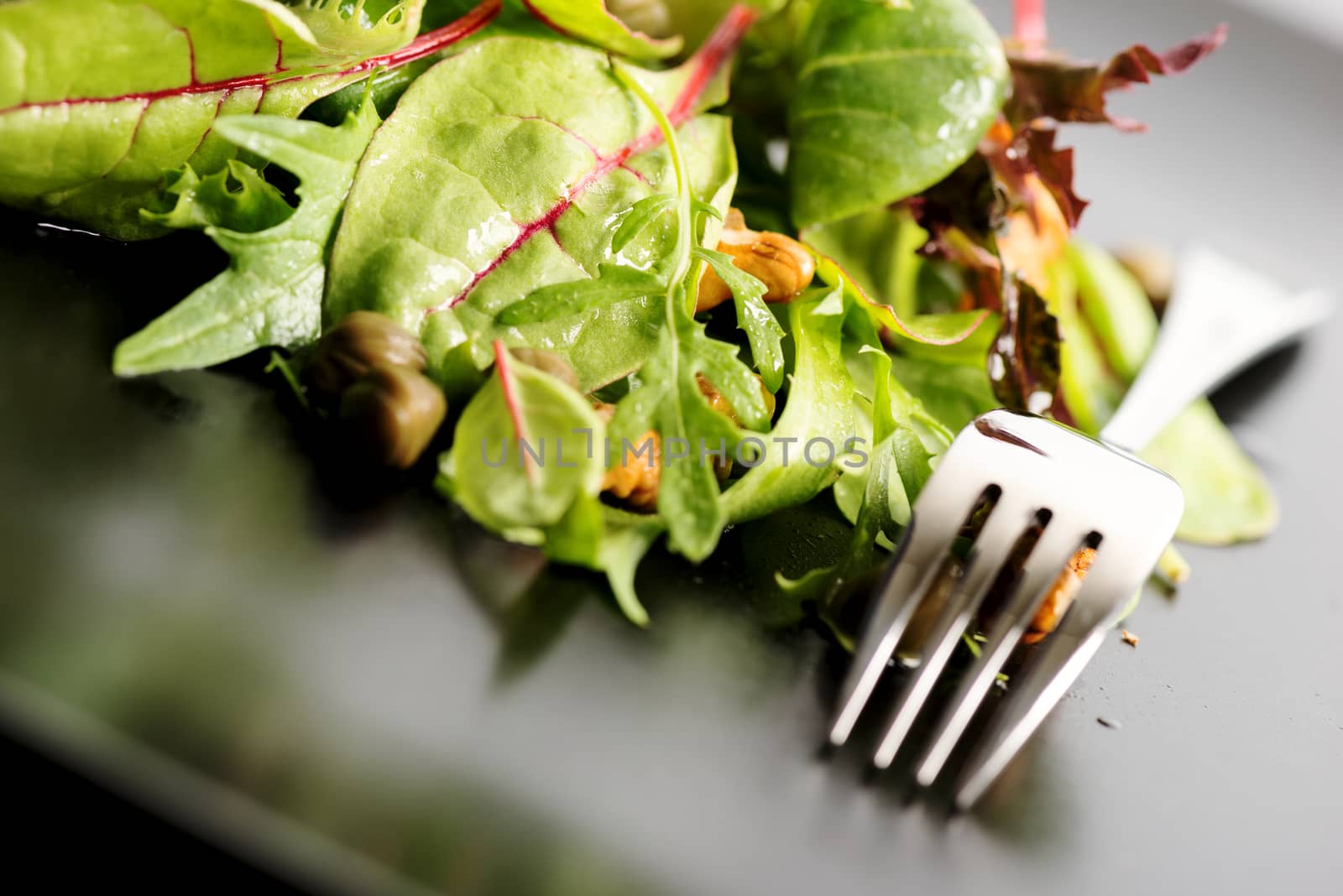 Fresh ecological salad mix with nuts on black plate, macro