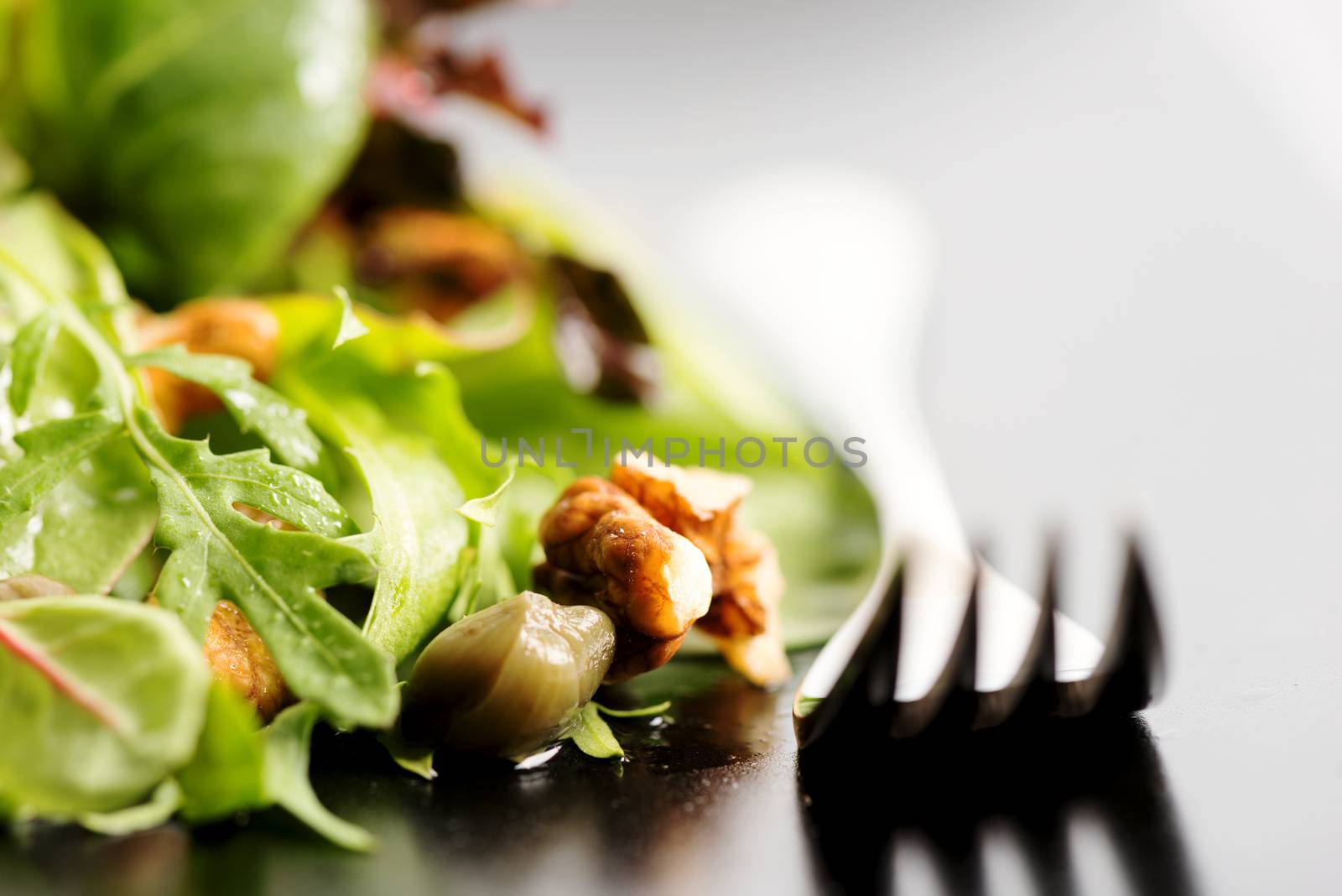 Fresh ecological salad mix with nuts on black plate, macro