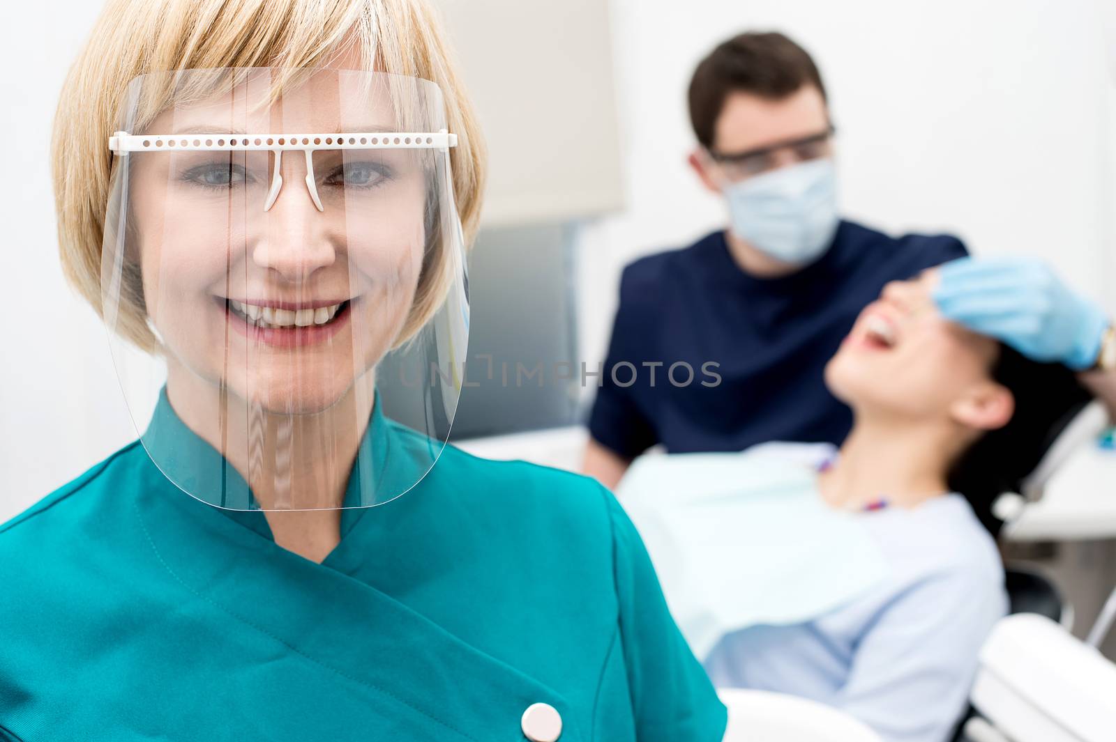 Woman assistant posing, behind dentist treating patient